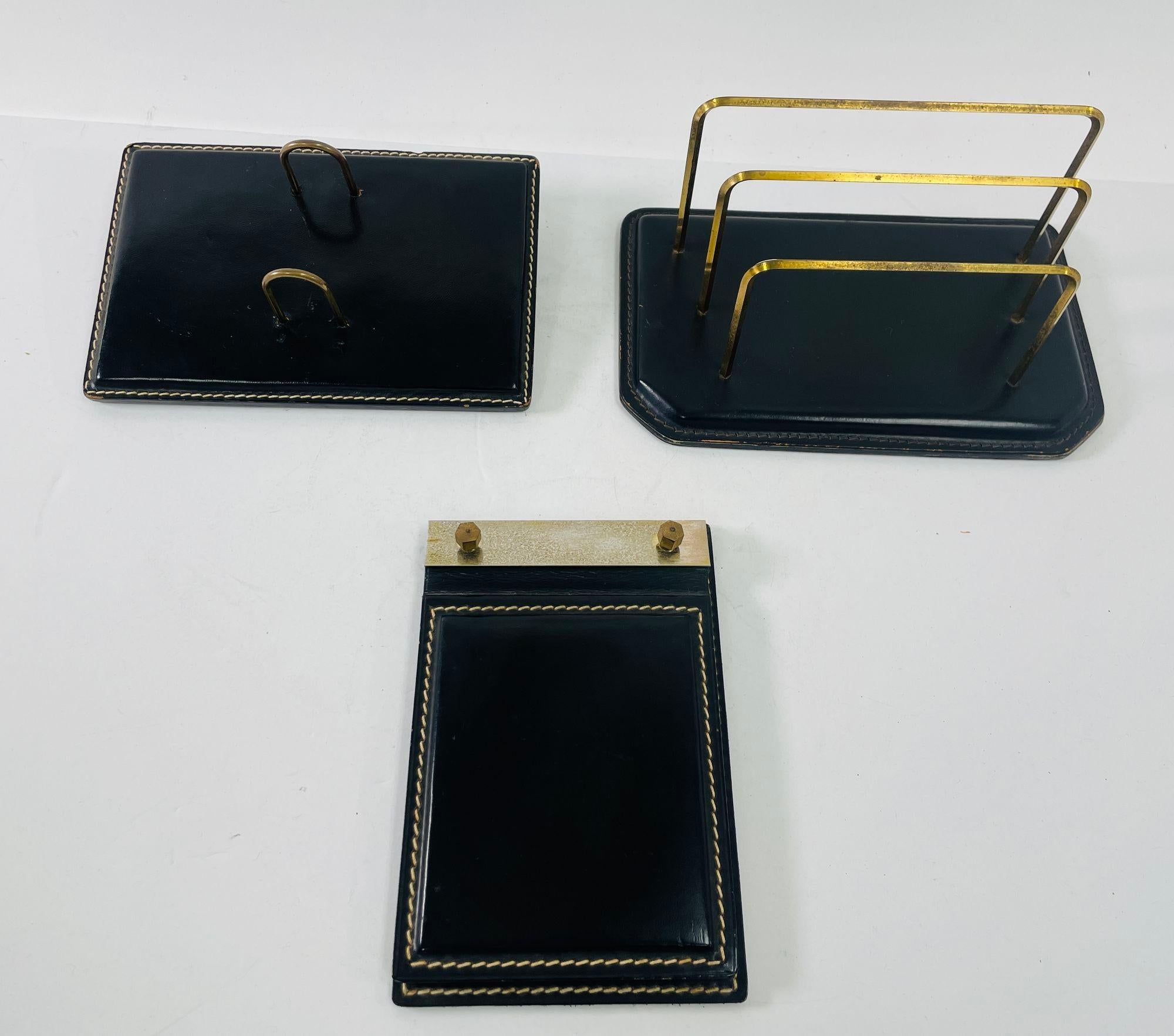 Vintage Jacques Adnet style Art Deco black leather saddle stitching with metal brass desk set.
A modernist desk accessories set designed by ILG, Belgium, in the 1950s. 
Art Deco style desk set comprising of a black leather and brass letter desk