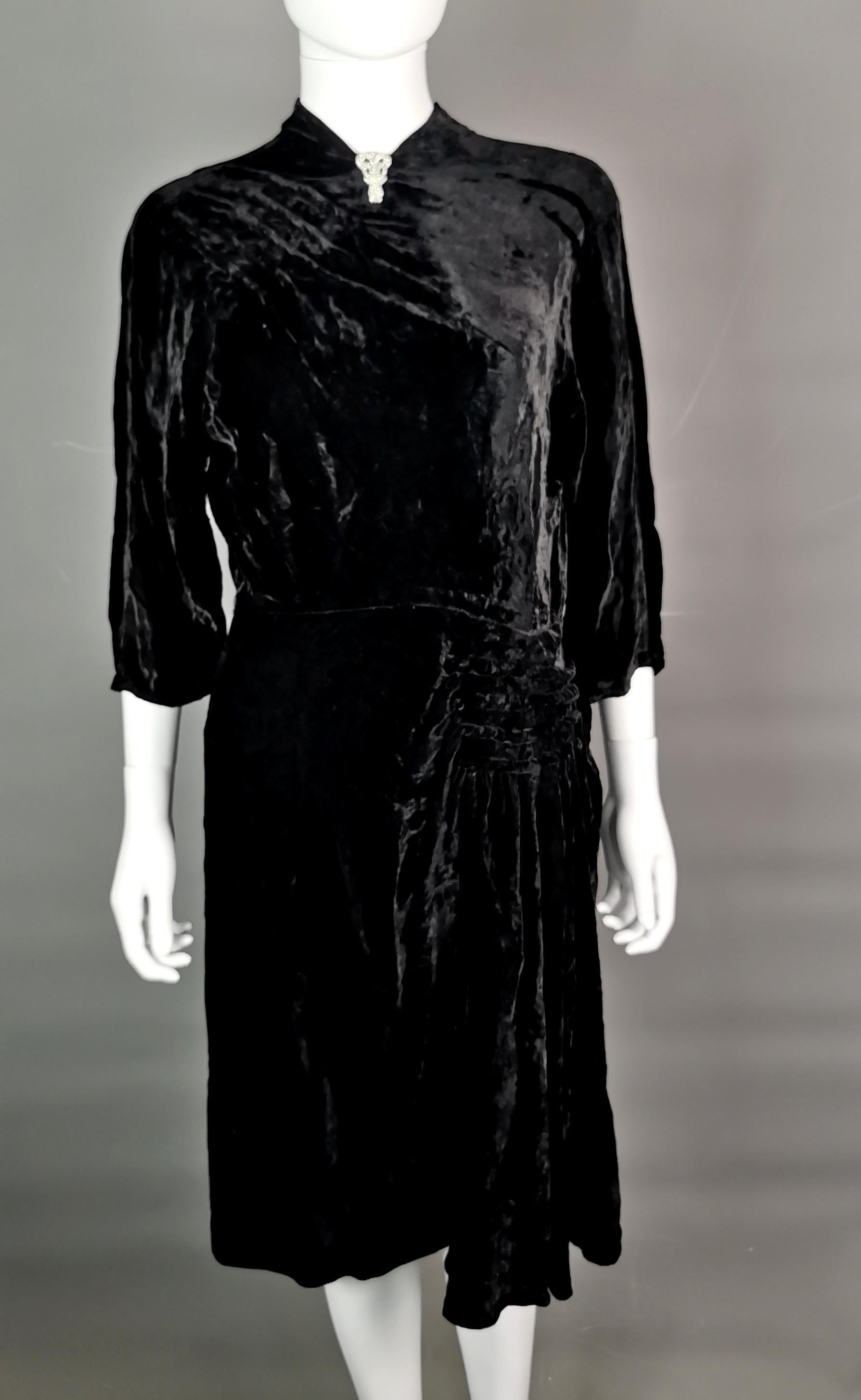 A gorgeous, vampy vintage 1930s Art Deco black velvet dress.

The dress has a very short cut out mandarin style collar with slightly sloped shoulders and the most gorgeous pin tuck pleat or ruching to the shoulder and hip on opposite sides.

A mid
