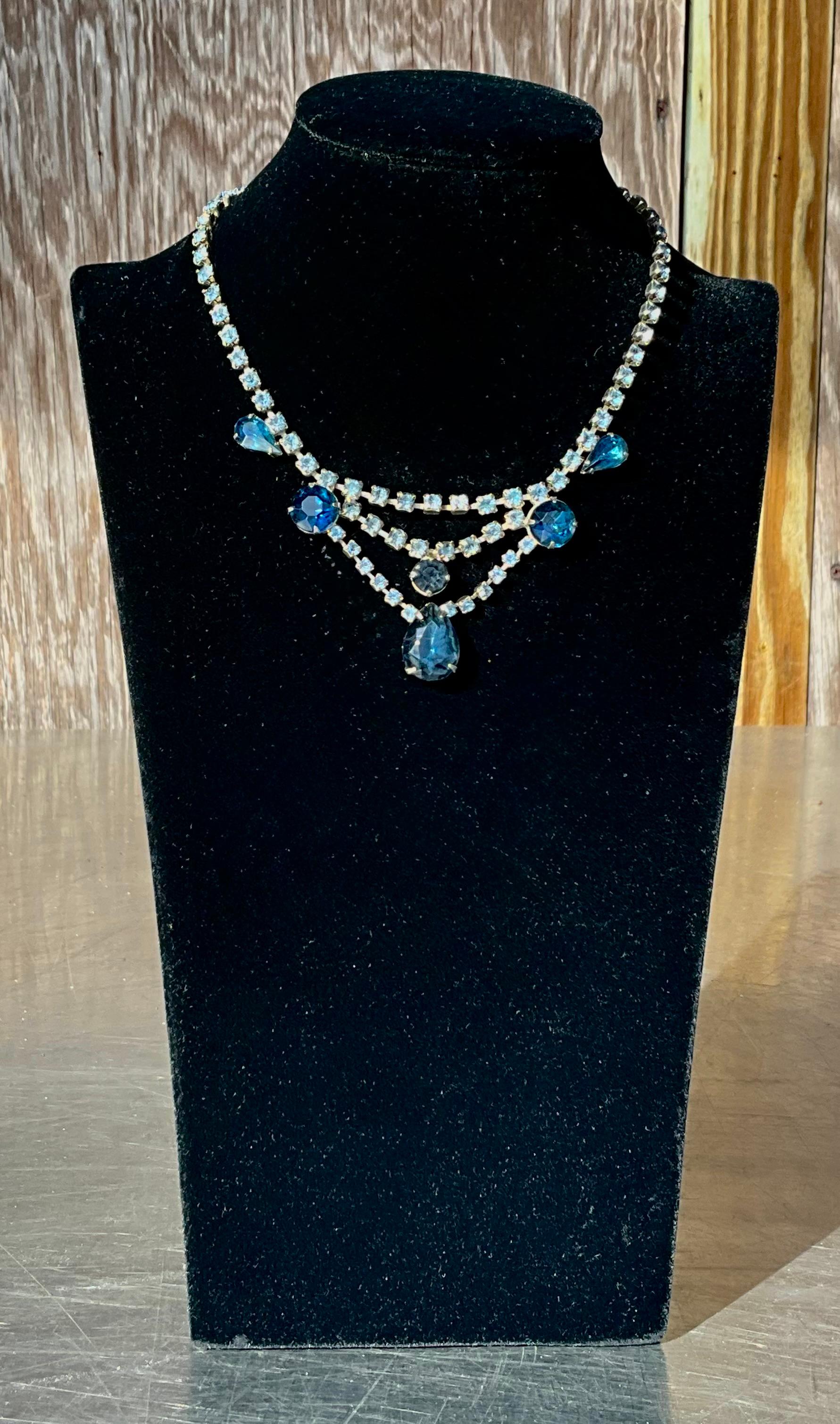 A Vintage Art Deco Blue Rhinestone Necklace is a stunning piece of jewelry that exemplifies the elegance and opulence of the Art Deco era, typically dating back to the early 20th century, around the 1920s to 1930s. This necklace would feature blue
