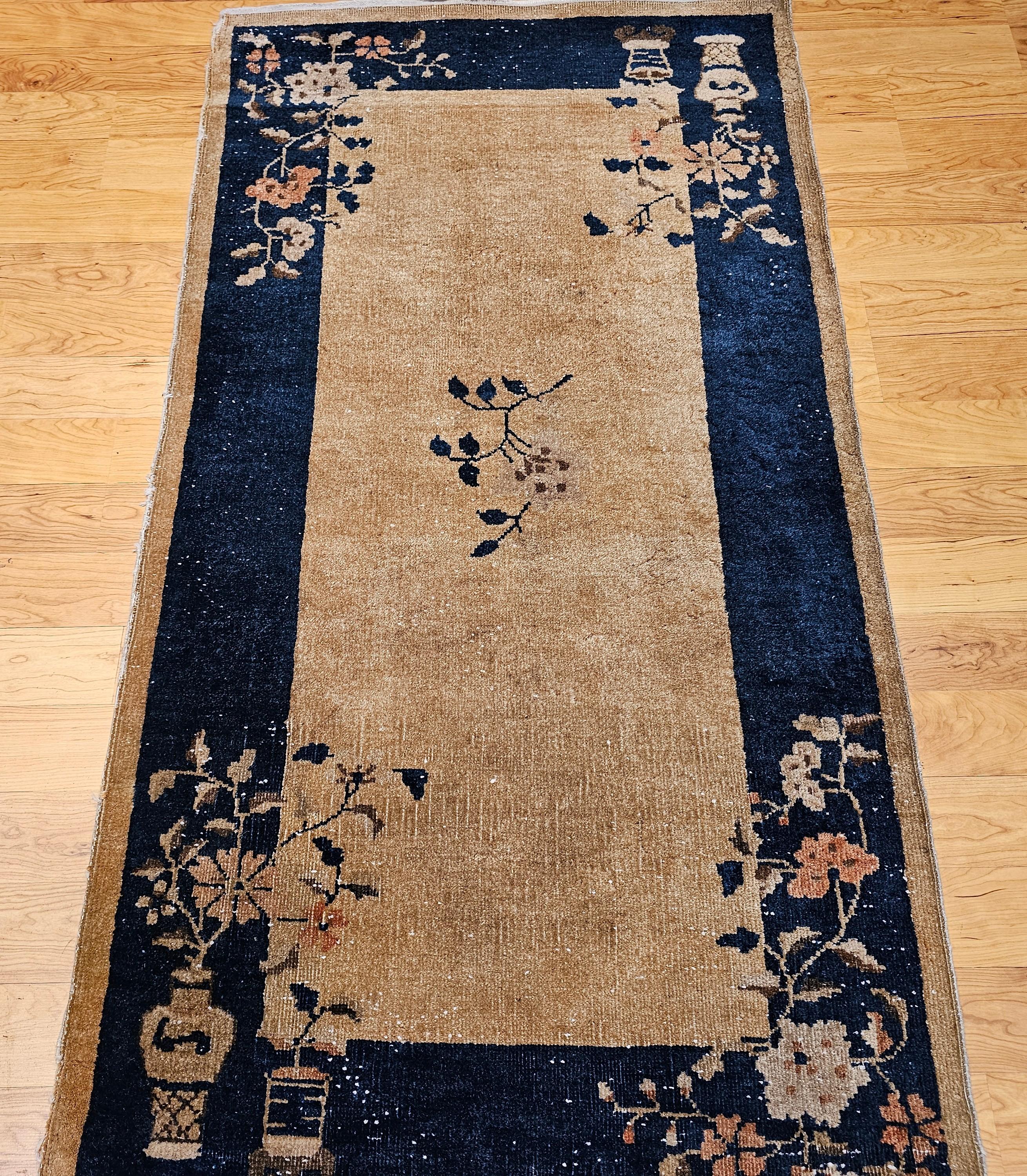 This vintage Art Deco Chinese area rug features a timeless and tranquil design, with a soft tan (cream-toned) field beautifully framed by a deep navy blue border. At the center lies a delicate floral medallion, while elegant flower vase motifs grace