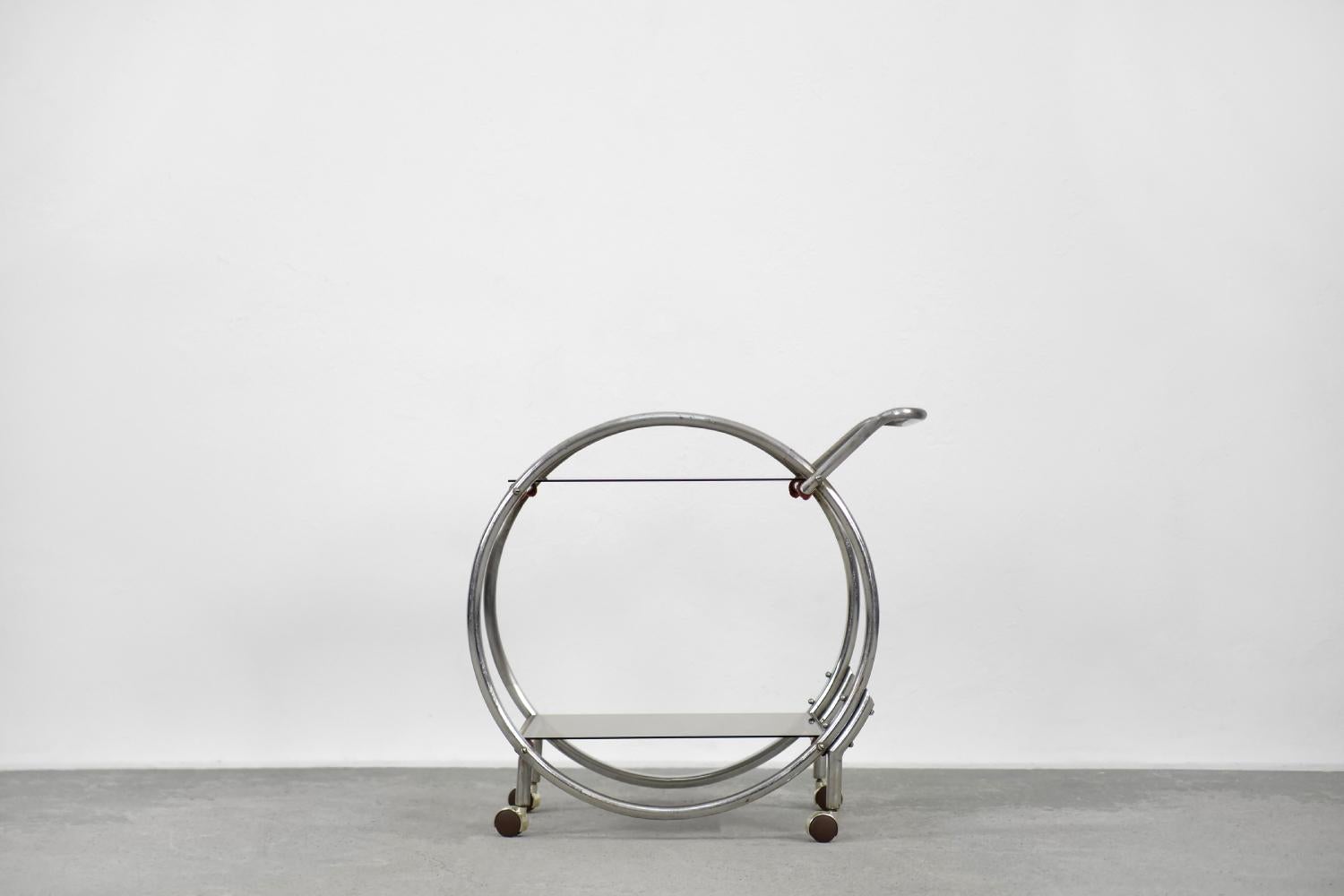 This two-level, circular bar table was made during the 1930s. This form refers to the designs of the Bauhaus school and the Art dèco style. The geometric frame is made of chromed tubular steel. This cart has two brown-smoked glass tops and mobile