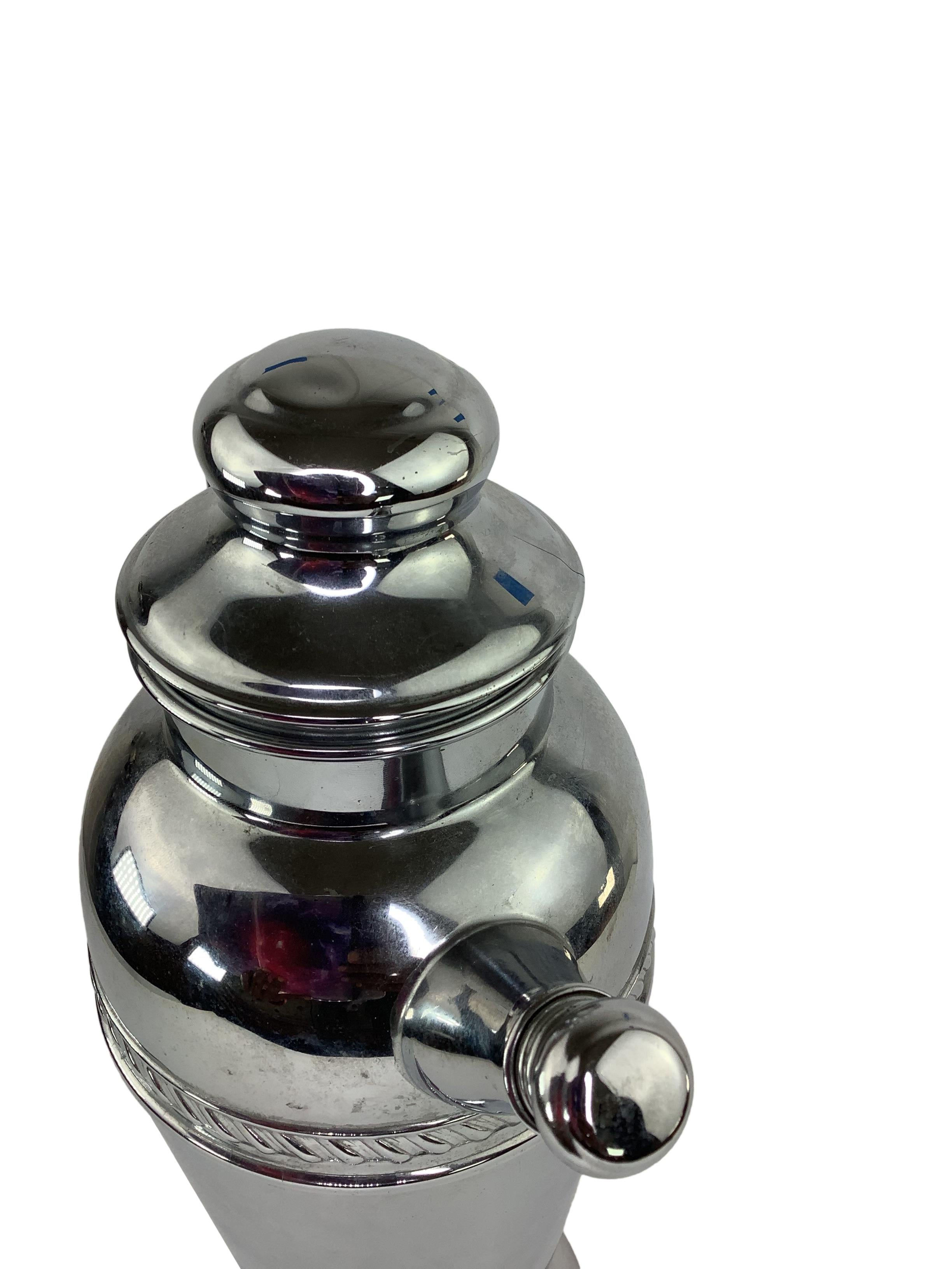 Vintage Art Deco Chrome Plated Cocktail Shaker. It's a relatively large shaker, which would have been used for mixing and serving cocktails. The chrome plating adds a shiny and luxurious appearance to the shaker, which is typical of the Art Deco