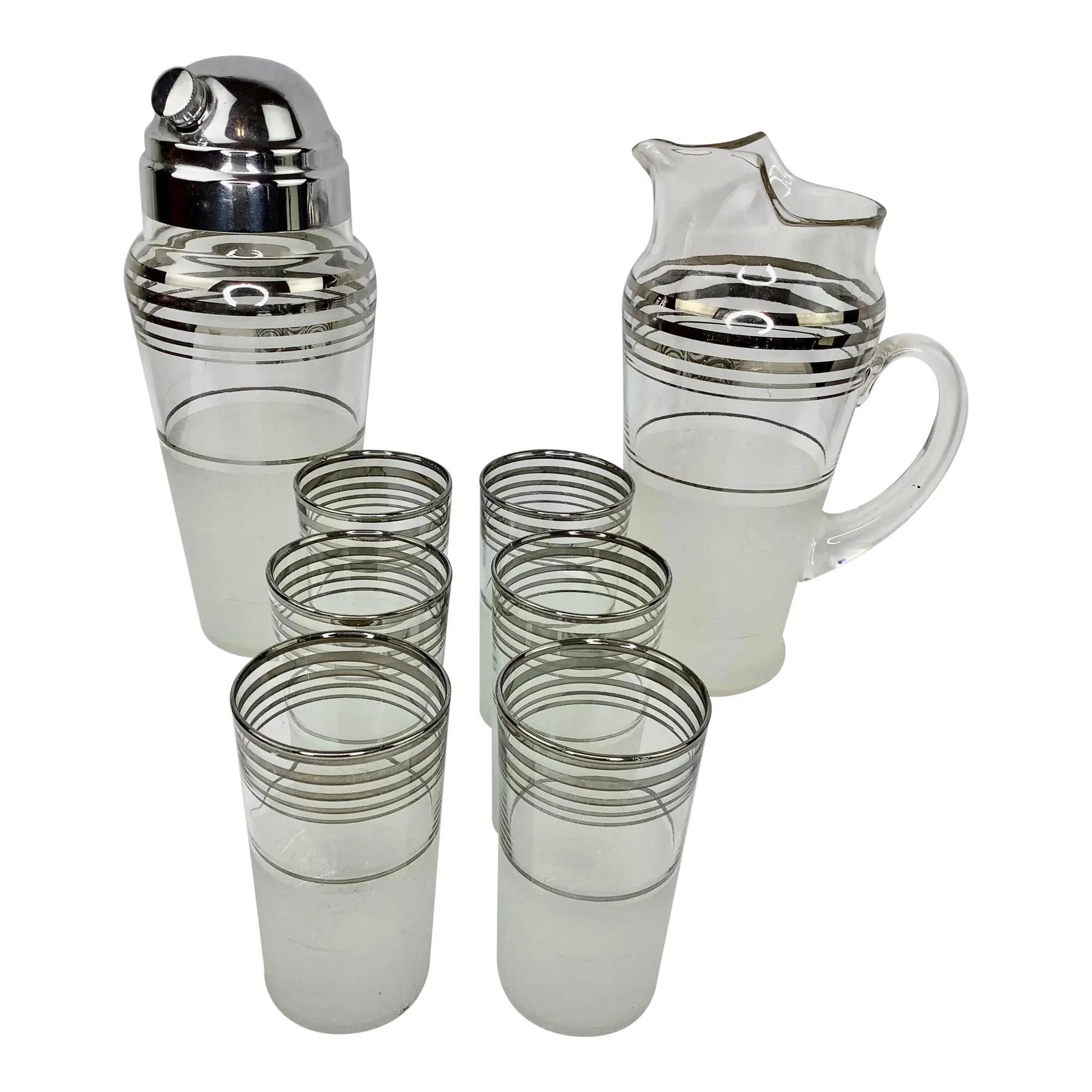 Juego de Cóctel Art Decó Vintage con Jarra, Coctelera Grande y 6 Vasos Highball. Cada pieza tiene bandas plateadas sobre cristal transparente encima de una sección inferior de cristal esmerilado. Los vasos miden 4 3/4