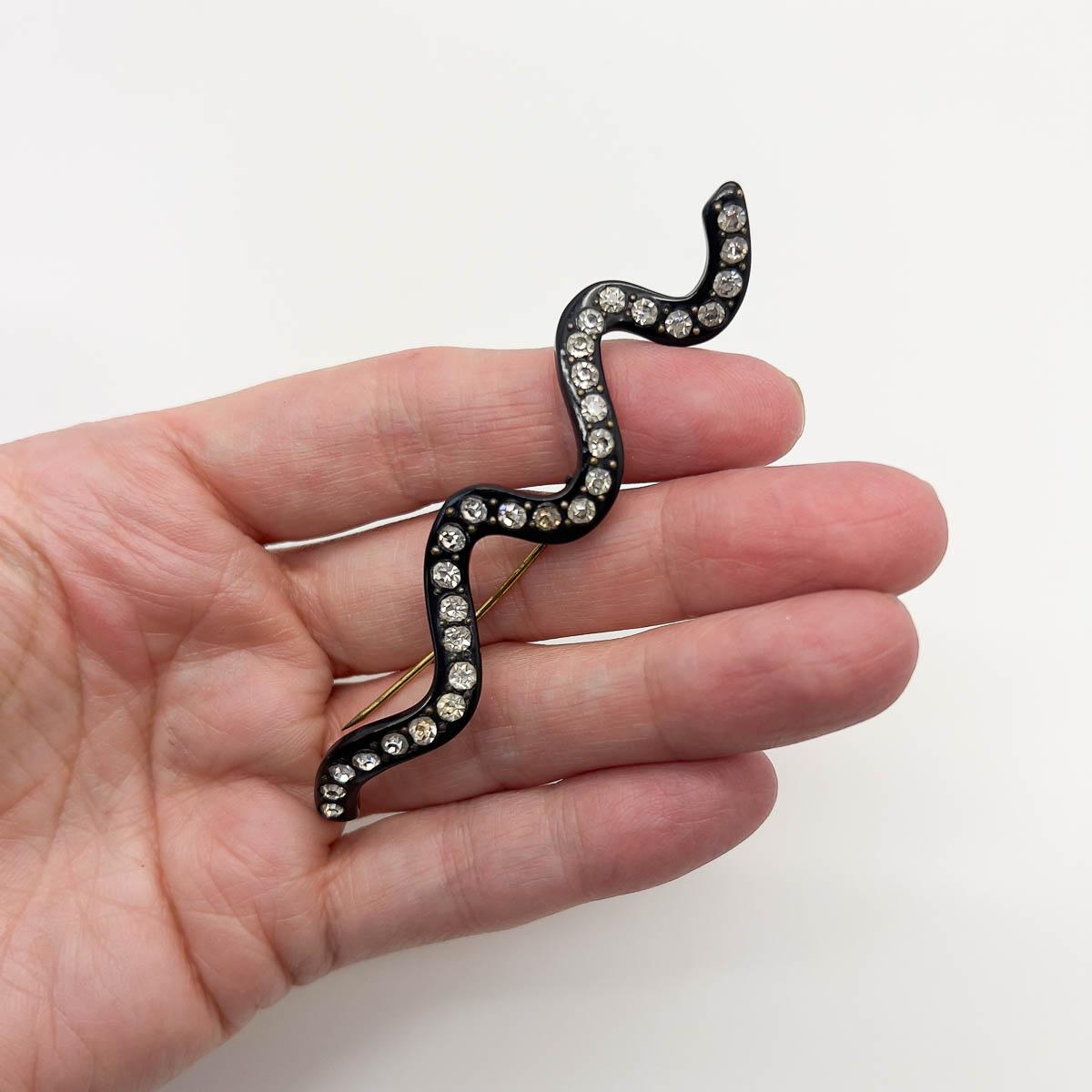 Eine Vintage Art Deco Schlangenbrosche. Schwarzes Bakelit, besetzt mit funkelnden Kristallen, ist ein schickes Schmuckstück, das ein ganzes Jahrhundert an Stil repräsentiert.

Eine unsignierte Schönheit. Ein seltener Schatz. Nur weil ein