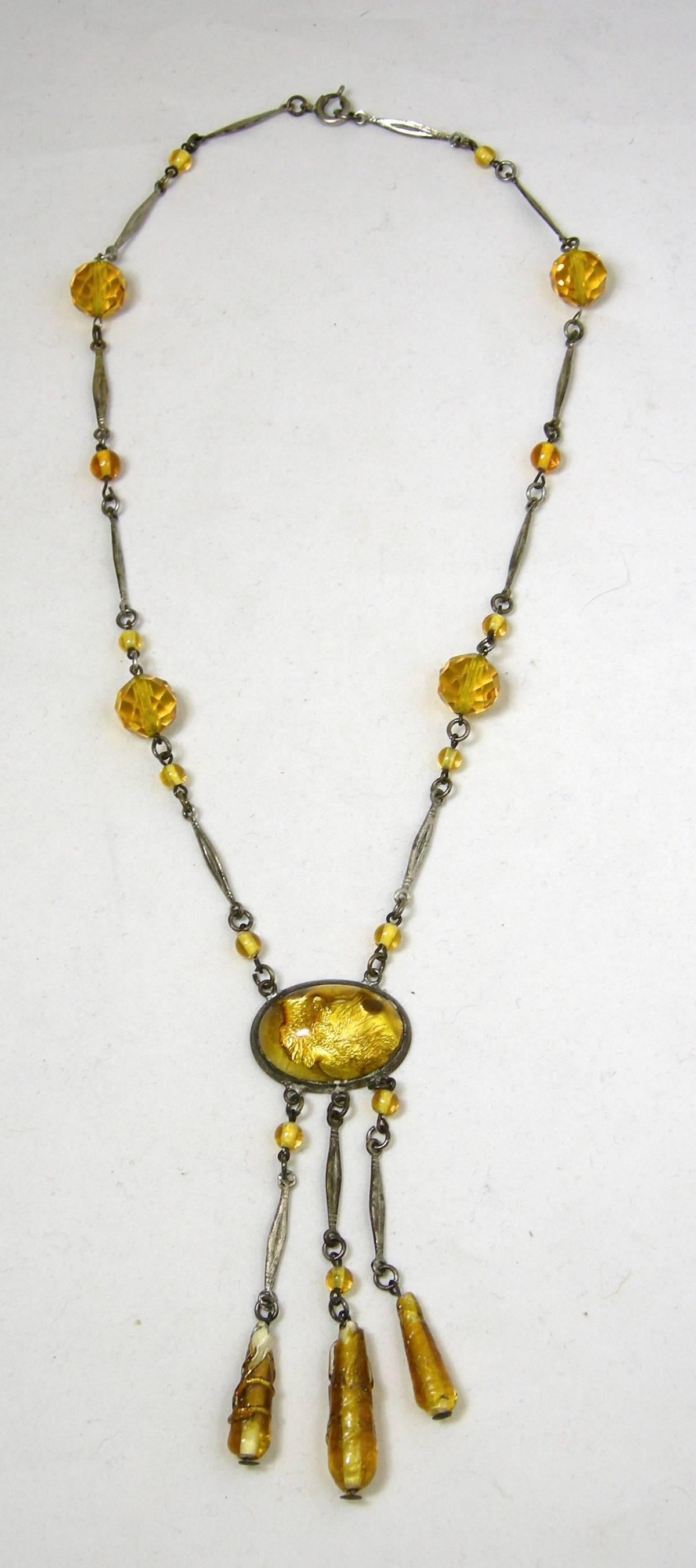 This beautiful early Czech necklace is in sterling or silver plate with stunning amber glass beads. The necklace is 17” long.  It has a mark, but I can’t make it out. The centerpiece is foil glass and measures 1” x 3-3/8” long with amber glass