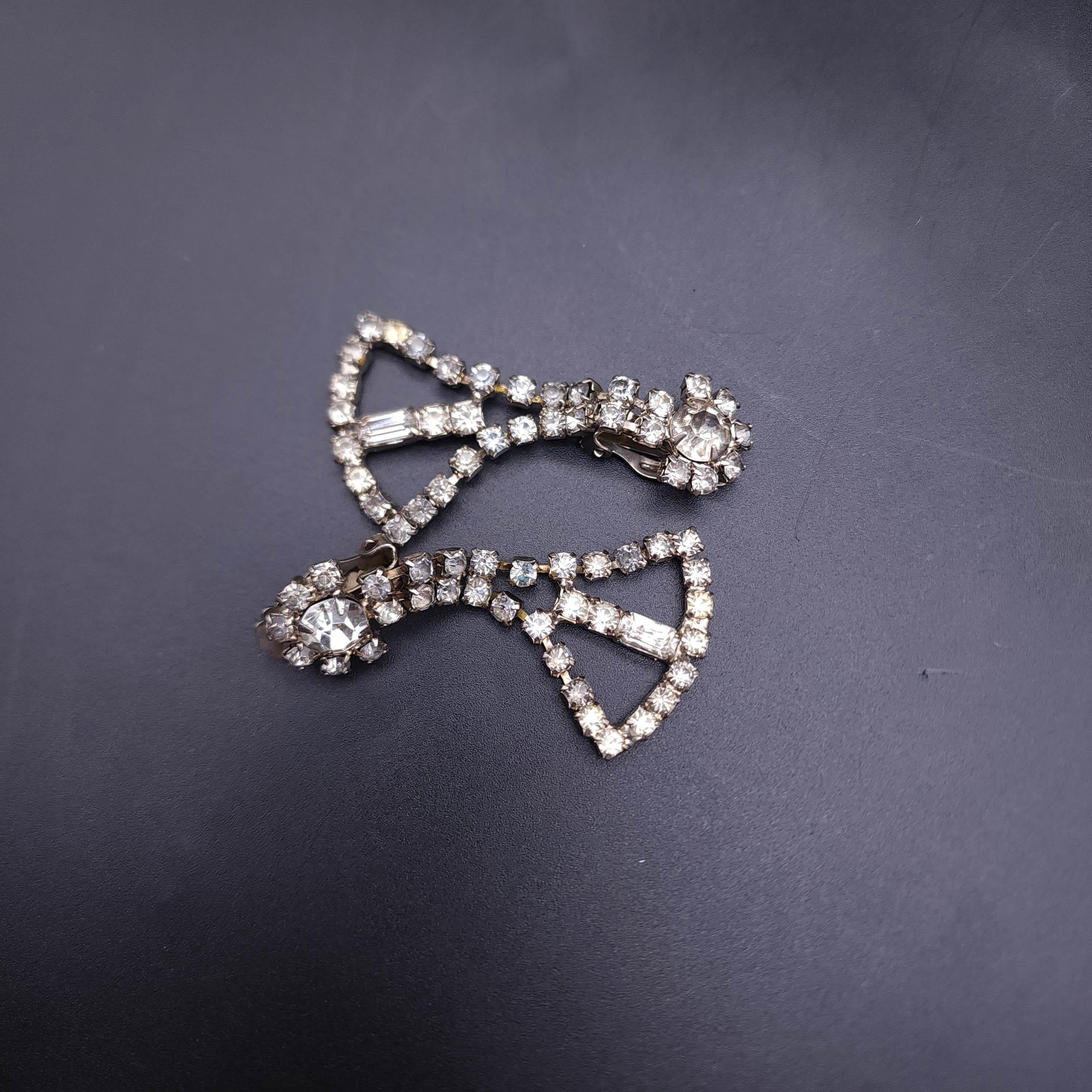 Step into the timeless allure of the Jazz Age with our vintage Art Deco dangling fan clip on earrings. These stunning pieces capture the essence of the 1920s with their classic fan shape and dazzling display of clear, prong-set sparkling crystals.