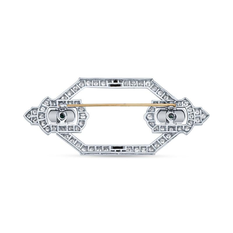 This estate brooch from the Art Deco period features approximately 3.50 carat total weight in Old European and Old Mine diamonds set in platinum. It is accented with onyx and two cabochon natural emeralds weighing approximately 0.40 carat total