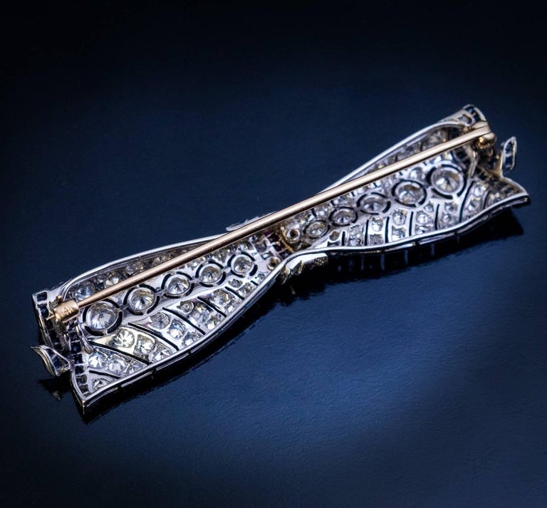 Circa 1930s
This vintage 14K white gold openwork brooch with a dynamic and flowing shape, is modeled as a diamond bow accented by channel-set rubies and sapphires. The brooch is embellished with a horizon of graduated old European cut diamonds