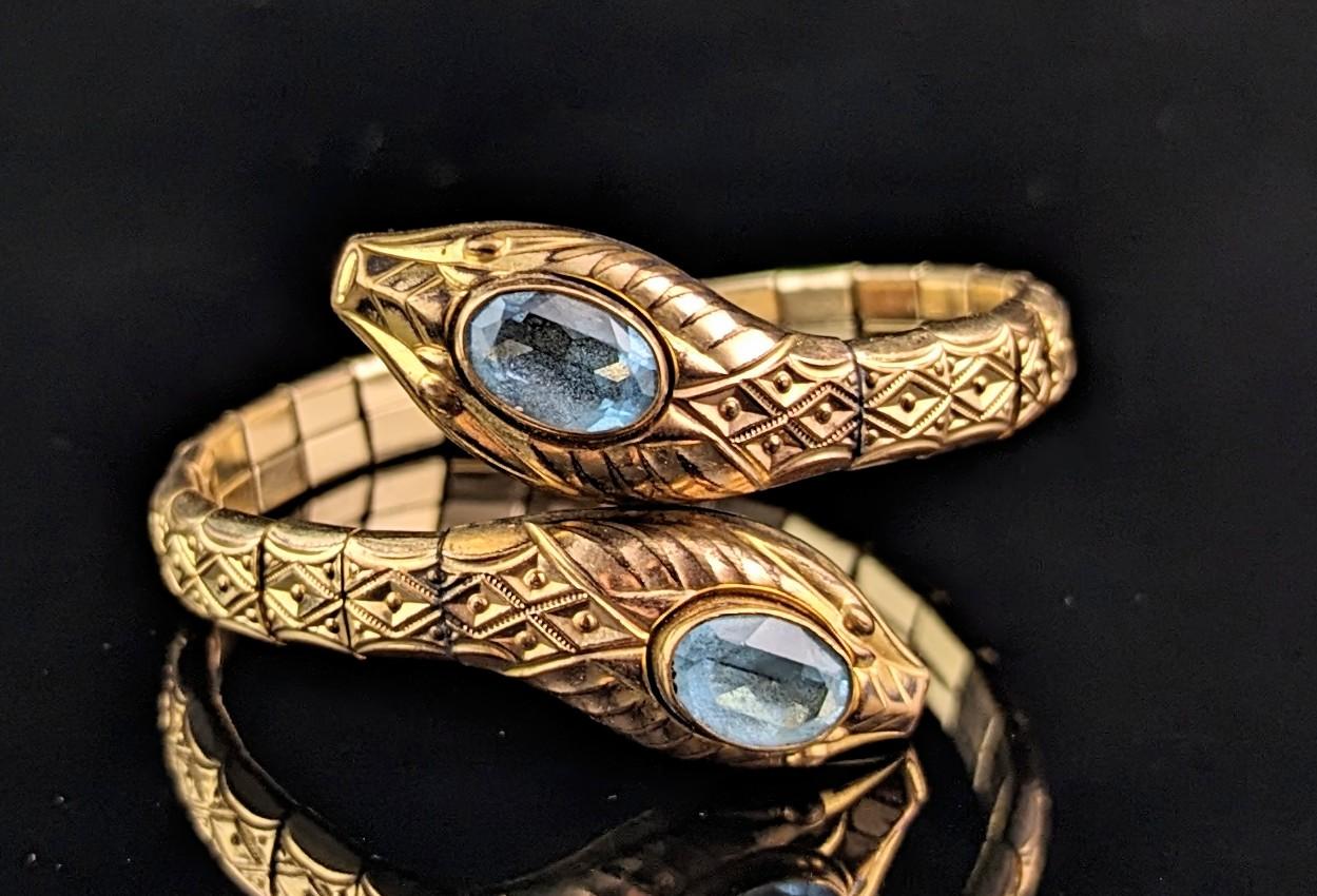 An amazing vintage, Art Deco double snake bangle or bracelet.

This gorgeous bangle is designed as two coiled snakes with a rich rolled yellow gold and textured, embossed body.

The heads of the snakes are set with large Aqua blue paste stones.

The