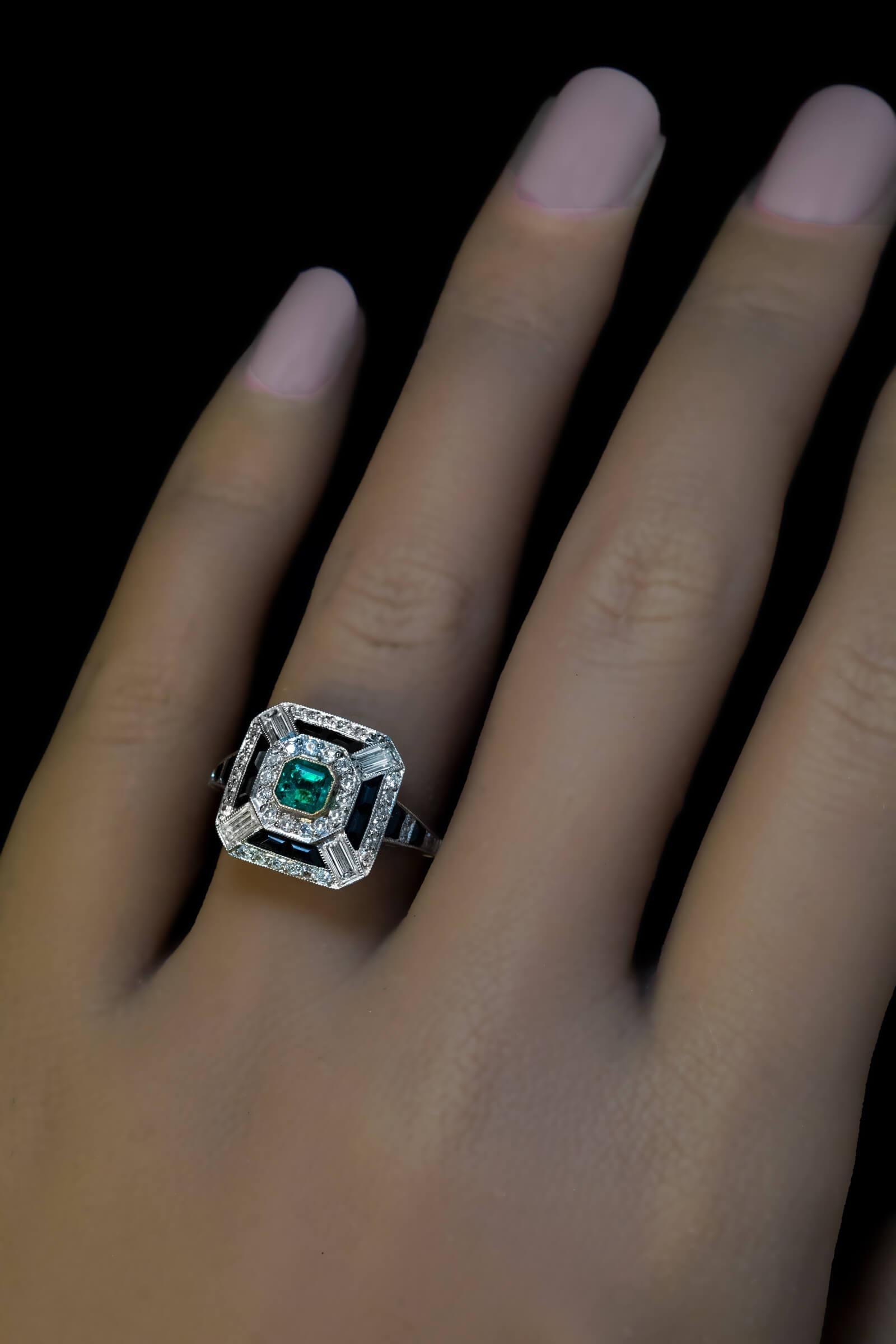 Circa 1920s  This elaborate pyramid shaped platinum ring of a bold Art Deco design is centered with a vivid bluish green emerald (likely Colombian) set in a yellow gold bezel. The emerald is framed by round and baguette cut diamonds and calibre cut