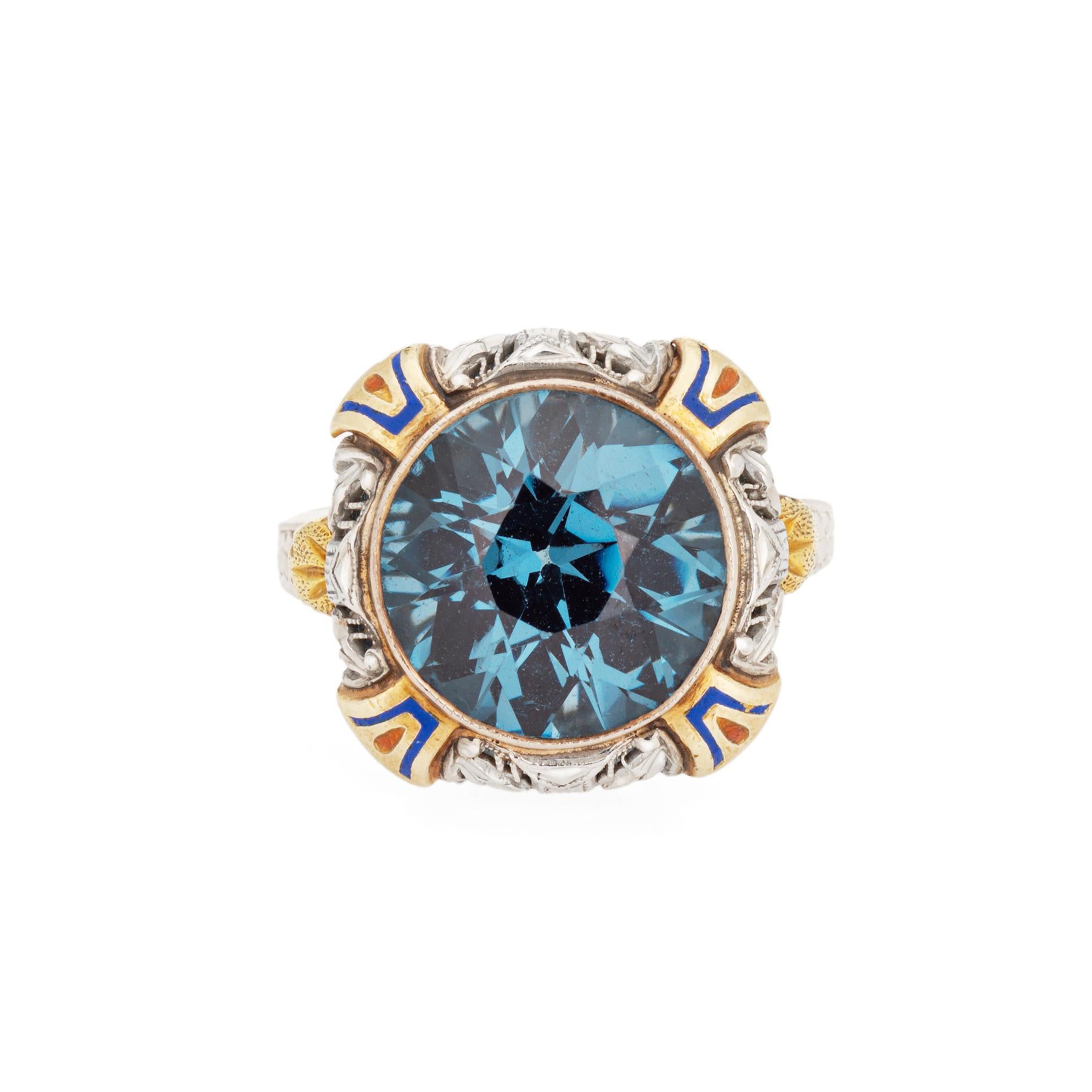 Vintage Art Deco era enamel cocktail ring (circa 1920s to 1930s) crafted in 14 karat white & yellow & white gold.

Blue and green enamel accents frame a faceted oval cut synthetic blue stone to the center, measuring 11mm. Note: few light surface