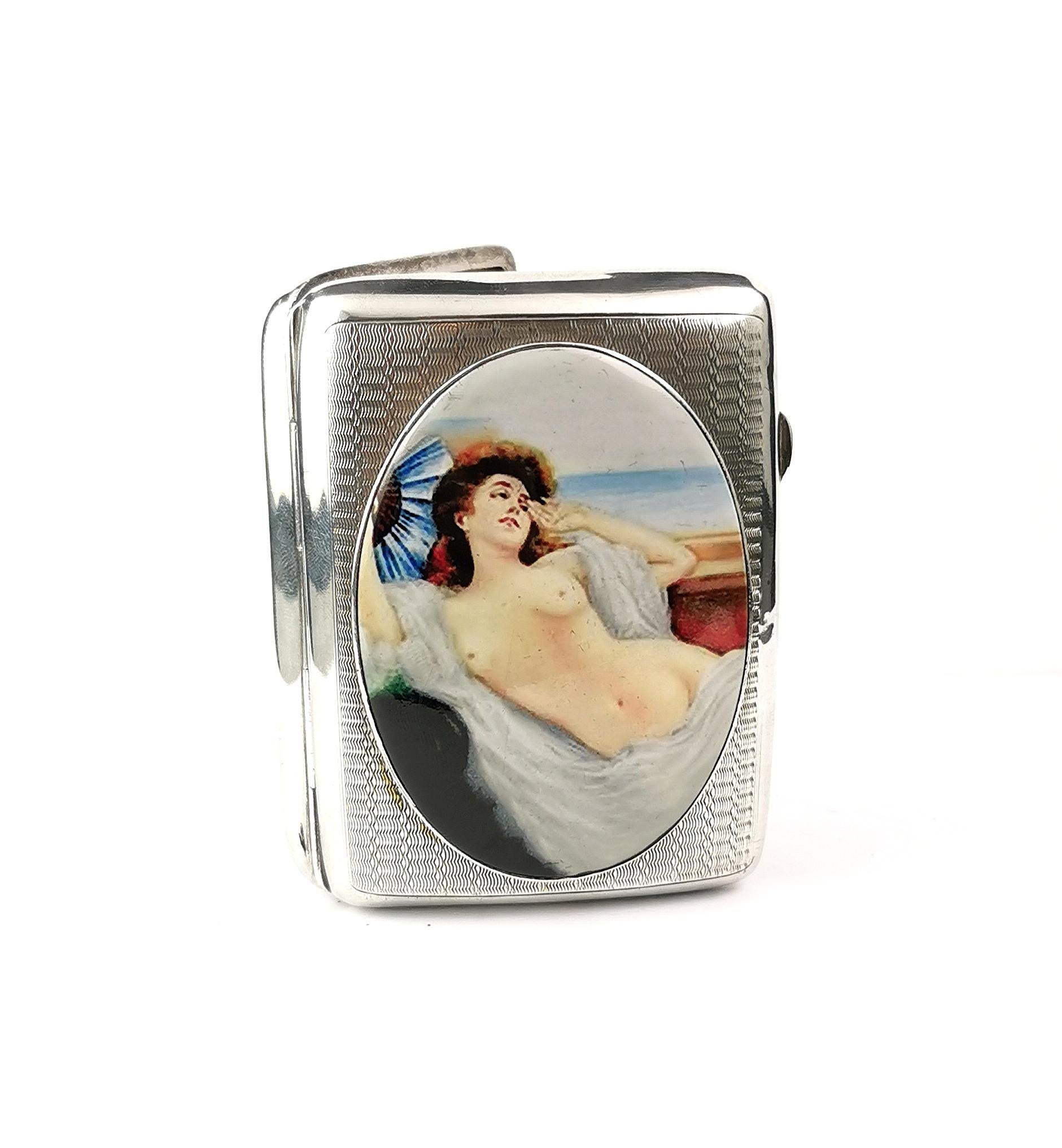 A beautiful vintage Art Deco era sterling silver and enamelled cigarette case.

The case has an erotic theme and features a lady topless in a reclined position with a fan and a gown.

The enamelled oval to the front is in good condition with no