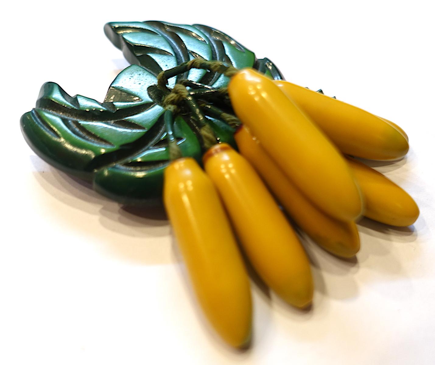 This famous  vintage Art Deco Bakelite brooch features 7 bananas suspended by green bakelite leaves. In excellent condition, this brooch measures 3-1/4” x 2-1/4” and has a c-pin clasp.