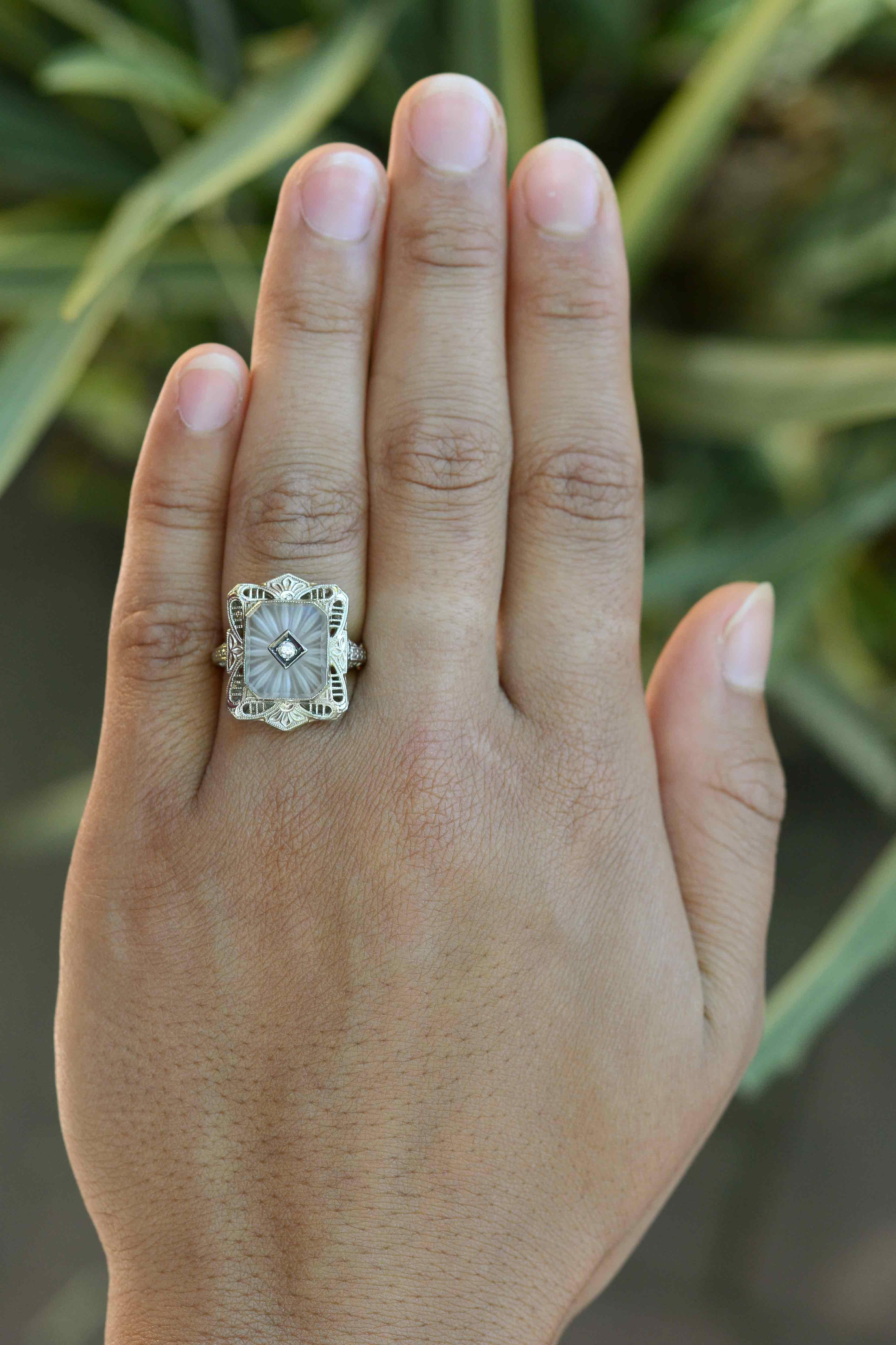 An elegant vintage Art Deco filigree engagement ring. Beaming from the center, a natural sun ray crystal radiates with a soft, frosty glow held within an architectural inspired frame with a shield shape. The lacy openwork dotted with dainty milgrain