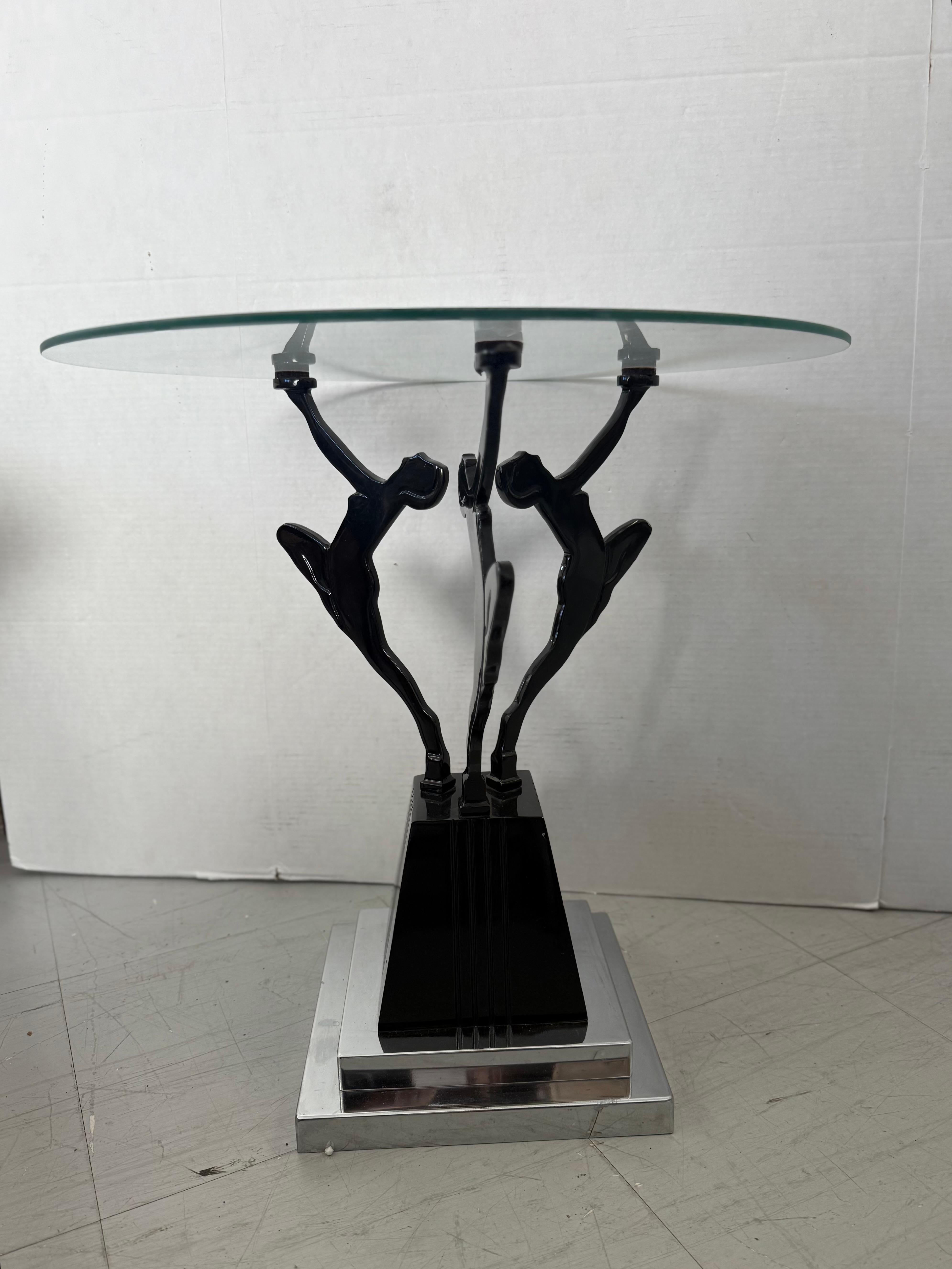 Von der Art Deco inspirierter Beistelltisch mit drei weiblichen Aktfiguren aus schwarzem Metall, die eine runde Glasplatte hochhalten. Der skulpturale Sockel ruht auf einem abgestuften, verchromten und schwarzen Sockel, der eine kühne Silhouette mit