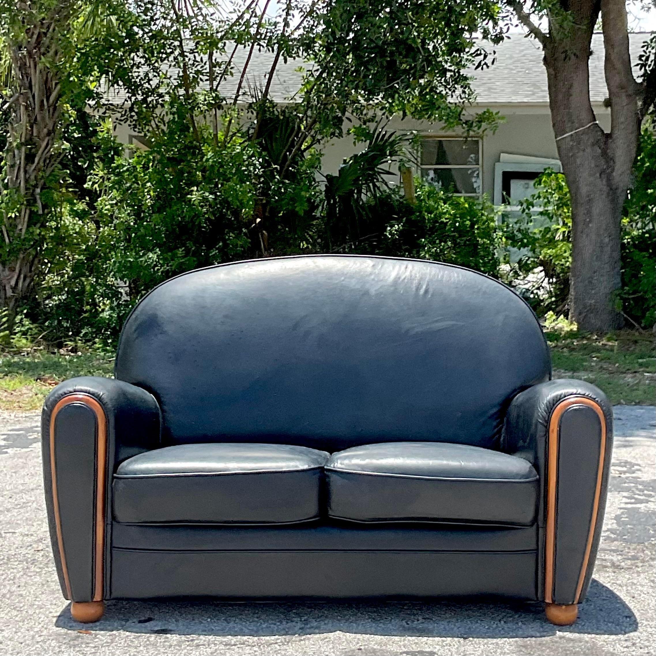 A fabulous vintage Art Deco loveseat. A chic black leather with wood trim. Acquired from a Palm Beach estate.