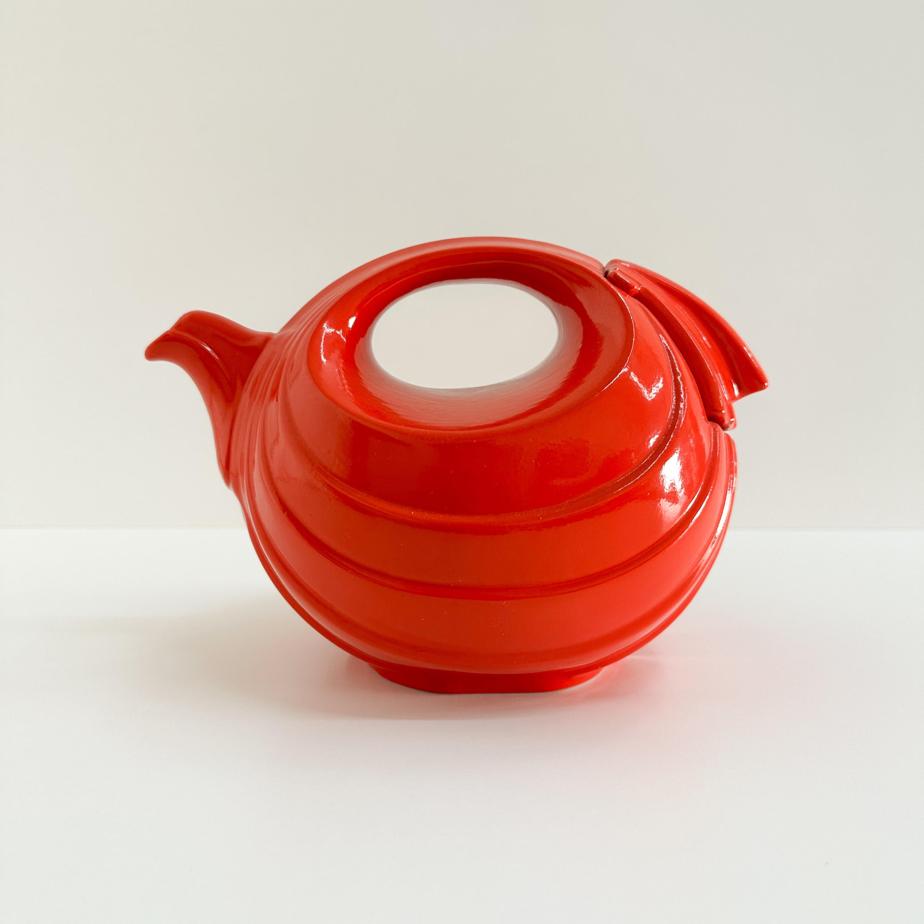 The Rhythm teapot design debuted in 1939. This example, identified by its backstamp, is a later production. Originally featuring gold detailing with upper drape accents, it was later offered in over 100 colors as part of the Hall American line.