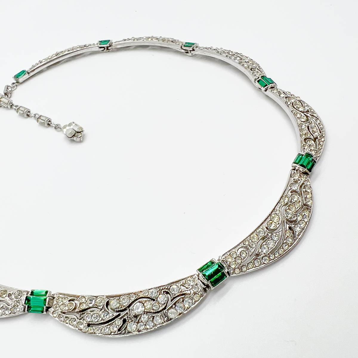 A Vintage Deco Style Emerald Necklace. This beautiful creation embodies the Art Deco period bringing emerald and white crystal together in an eternally stylish design featuring scalloped, pattern cut panels. Finished with a crystal embellished hang