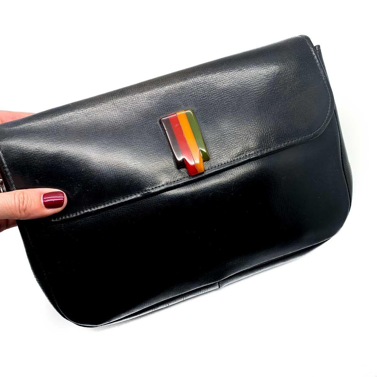 A Vintage Art Deco Bakelite Clutch Bag from the 1930s. An eternally classic black leather clutch finished to perfection with the hallmark art deco Bakelite in four glorious colours. A stylish grab strap on the back makes carrying easy and elegant. A