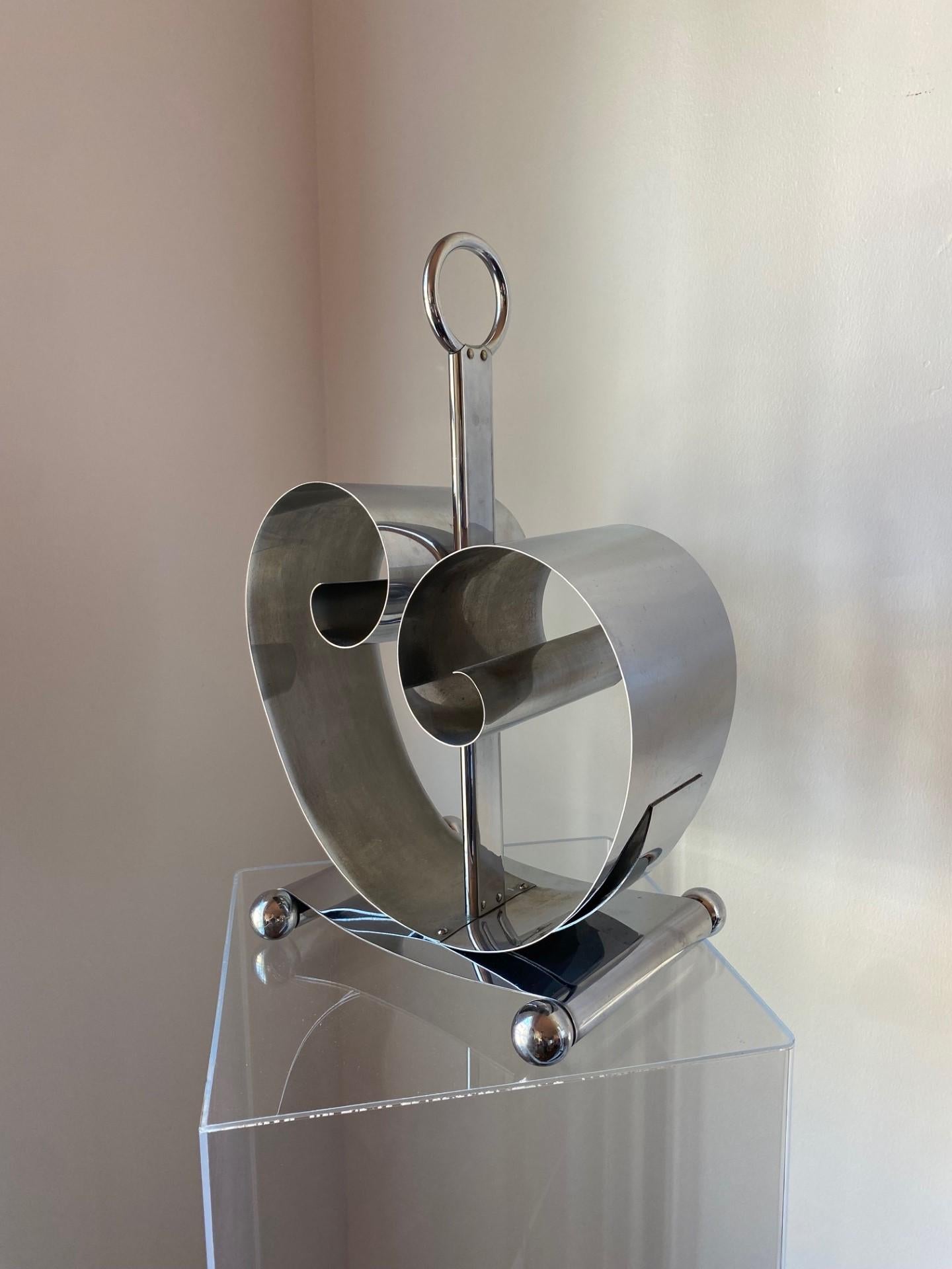 Sculptural and unique.  Beautiful industrial era, chrome spring steel magazine rack designed by Fred Farr for Revere of Rome, NY.  Two undulating metal sheets act like coils against a central base shaft with a ring handle, creating tension which