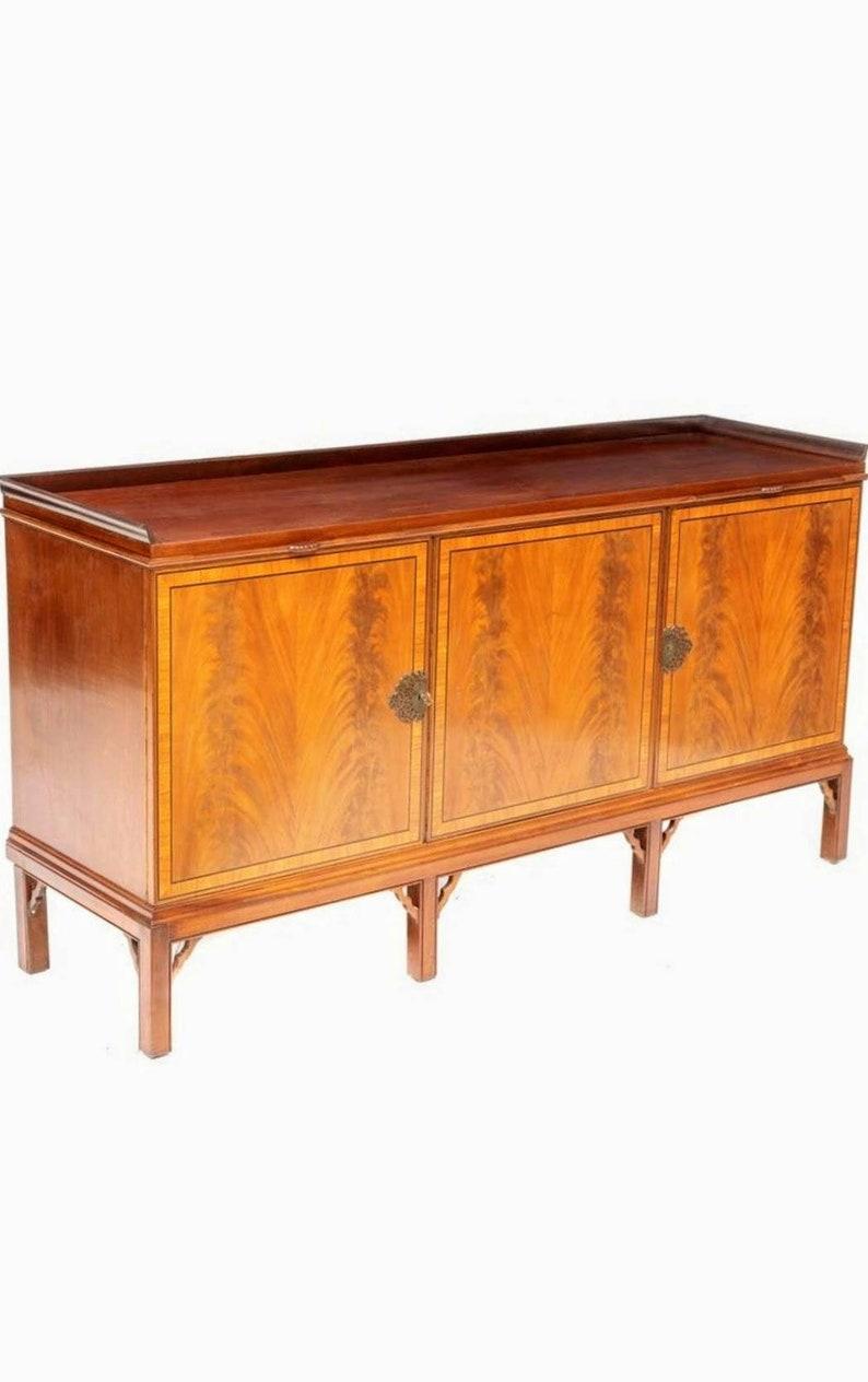 A vintage, circa 1930s, Art Deco Moderne period mahogany sideboard, with stunning cross banded inlay framed highly figured flame mahogany panels. 

Born in the early/mid 20th century, having a rectangular server top with partial raised gallery,