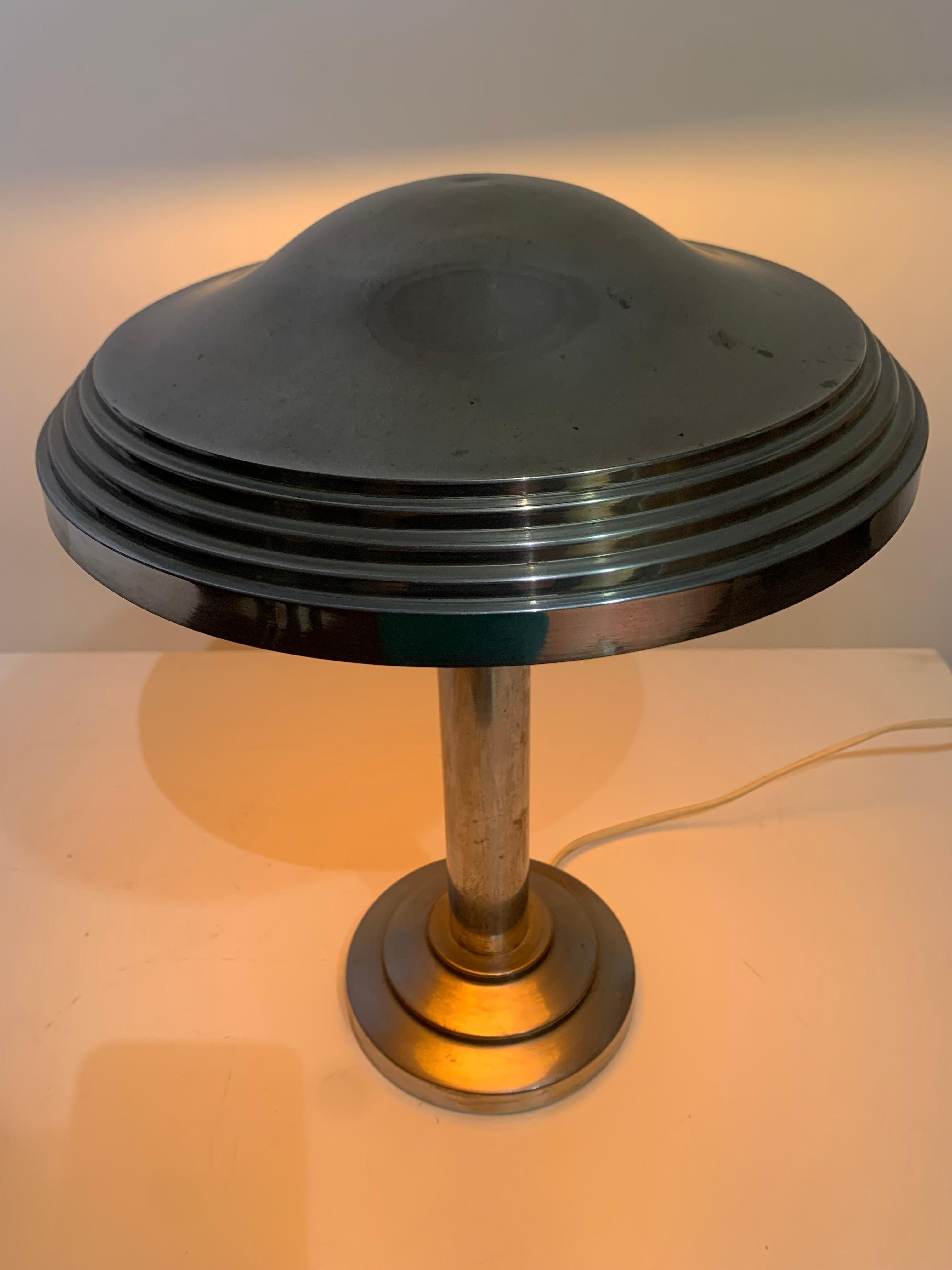 An Atomic Age/Art-Deco table or desk lamp with an attached saucer shade mad from chrome-plated steel.
Typical item from the mid-century, this lamp is a statement piece and is absolutely gorgeous. 
The lamp has been rewired with new chords by a