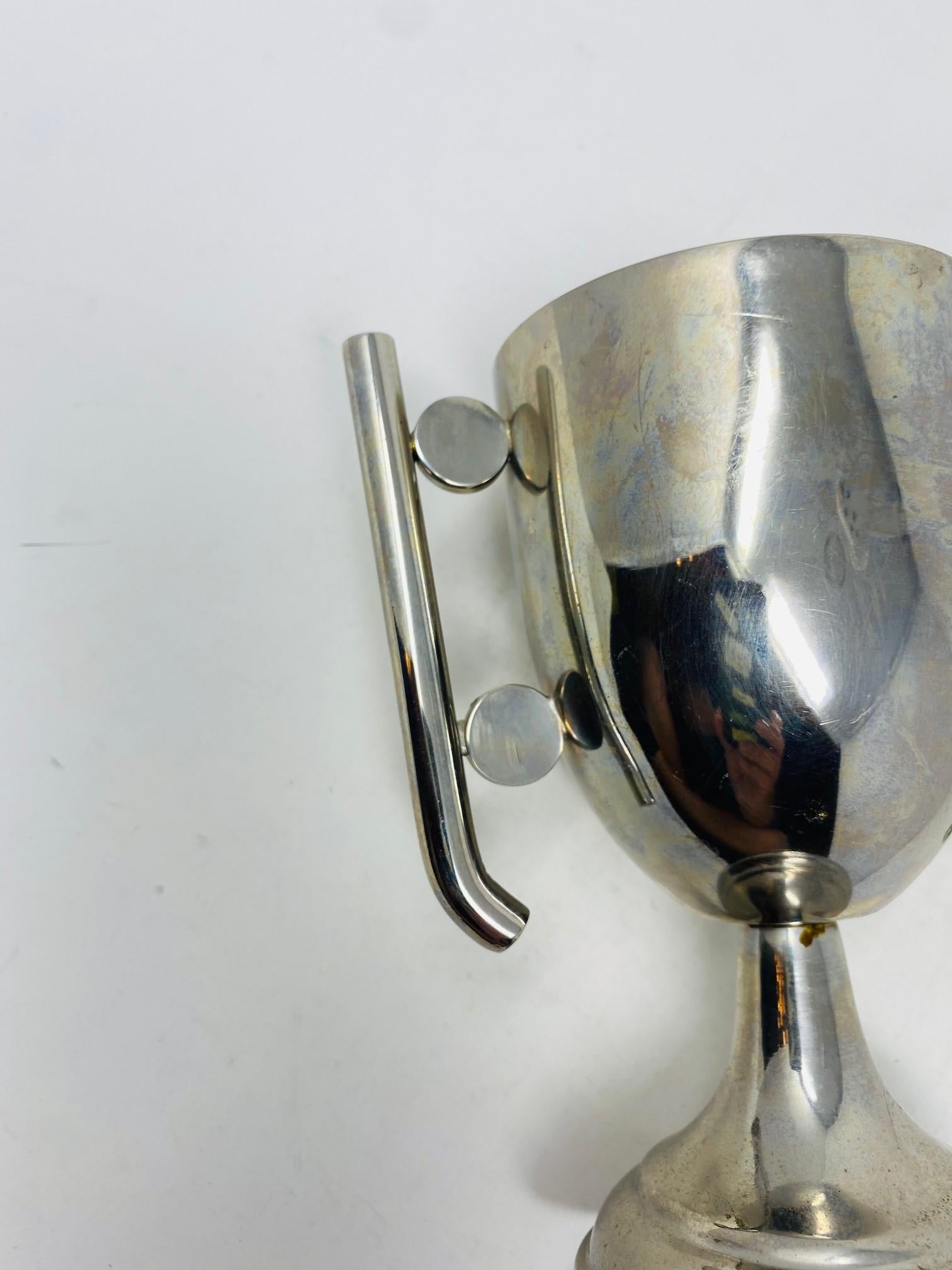 Un trofeo incredibilmente minimale e scultoreo che emerge come una scultura.  Questo pezzo classico presenta uno stile art déco e chic.  Le linee minimali della tazza sono esaltate dagli elementi semicircolari che contengono i manici.  Stile e