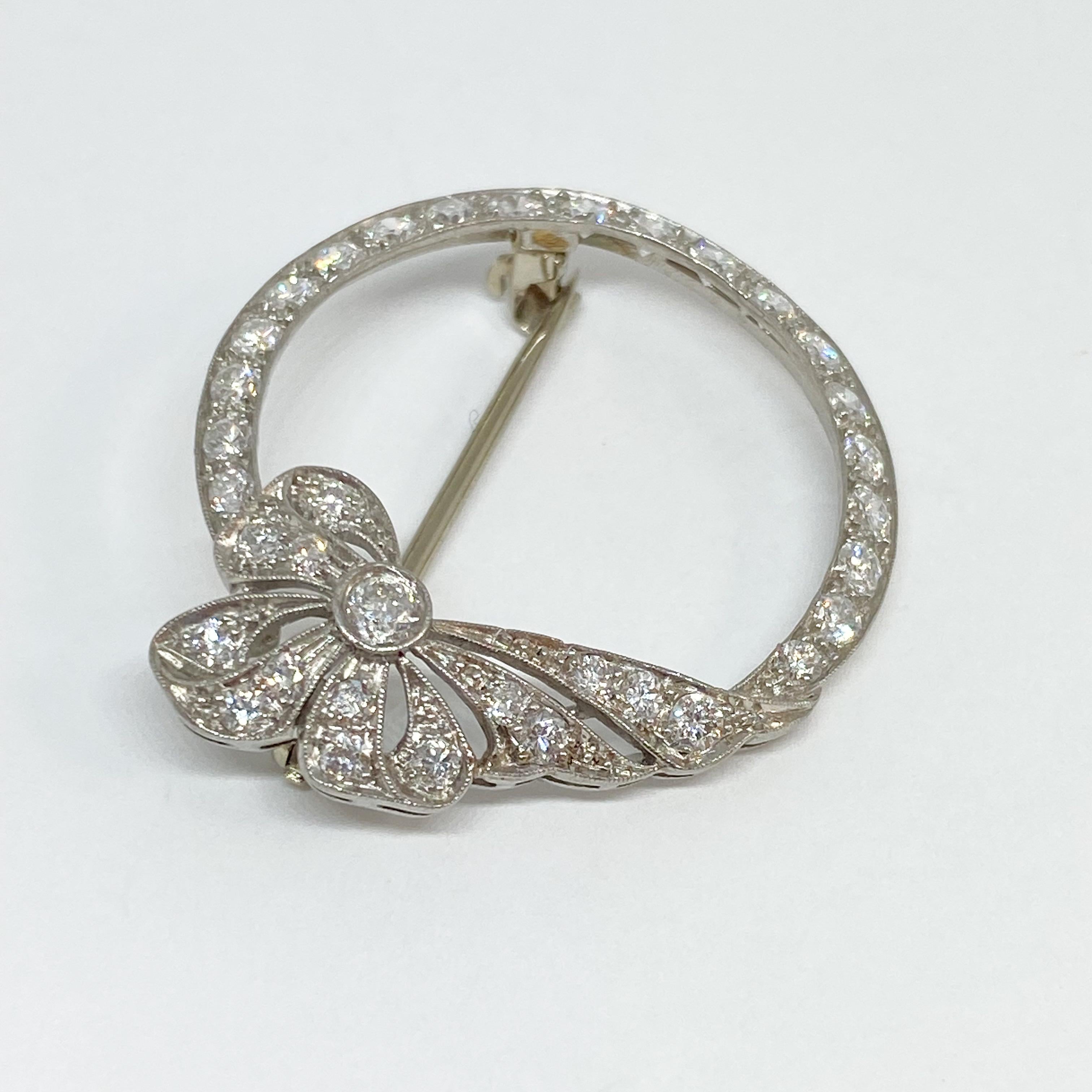 Vintage Art Deco brooch pin set with Old European cut and transitional cut diamonds. Designed in platinum with a ribbon circle motif, hinged pin brooch and catch. The diamonds have a combined total weight of 1.45 carats, G-H color, VS clarity. The