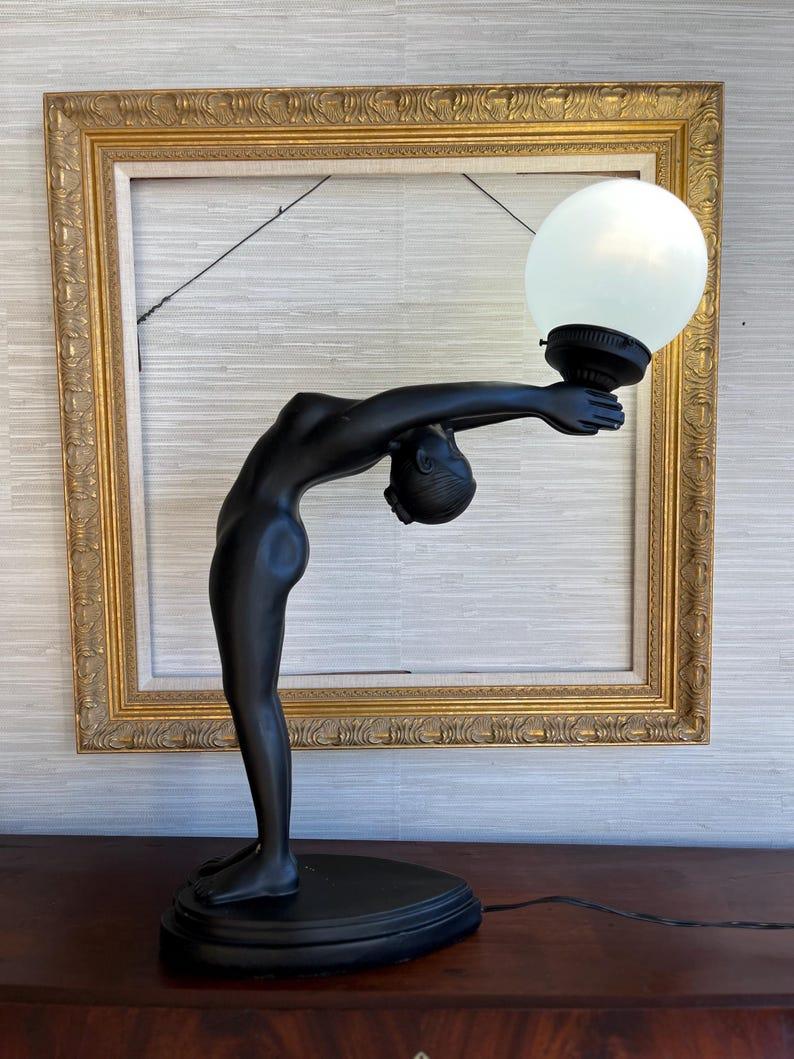 Questa splendida lampada in stile Art Déco dona un'eleganza senza tempo a qualsiasi ambiente. Ispirato alle iconiche opere di Max Le Verrier, presenta una graziosa donna nuda in equilibrio sulla punta dei piedi, protesa all'indietro mentre solleva
