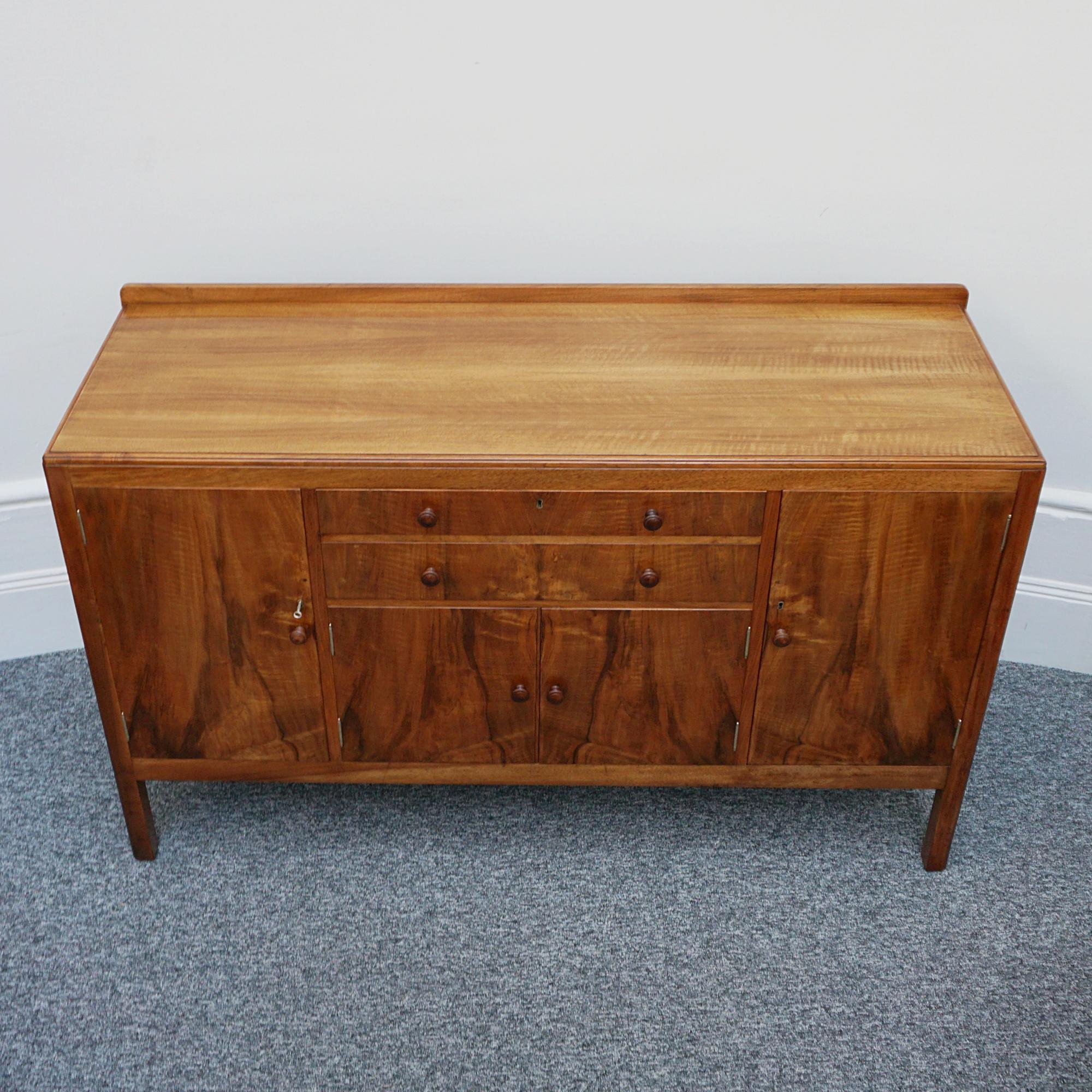 An Art Deco sideboard by Heal's of London. Burr walnut and figured walnut veneered with original walnut handles. Two central upper drawers with lower cupboard compartment flanked be two shelved cabinets.

Dimensions: H 92cm W 101cm D 52cm

Origin: