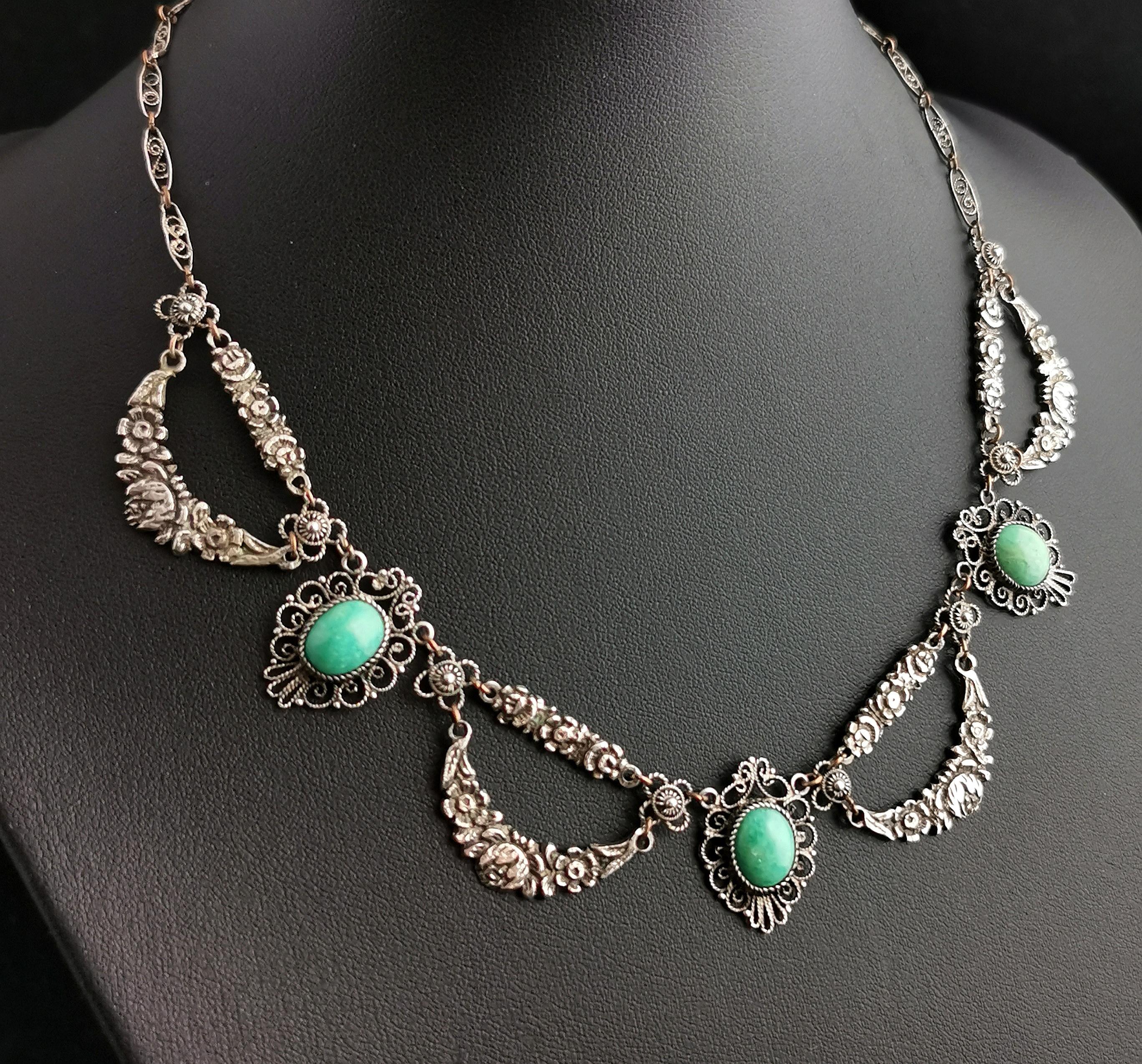 A beautiful vintage Art Deco silver and Amazonite festoon style necklace.

This pretty necklace is designed with delicate silver filigree links, intercepted with repousse floral panels.

It has three carved and polished Amazonite cabochons set into