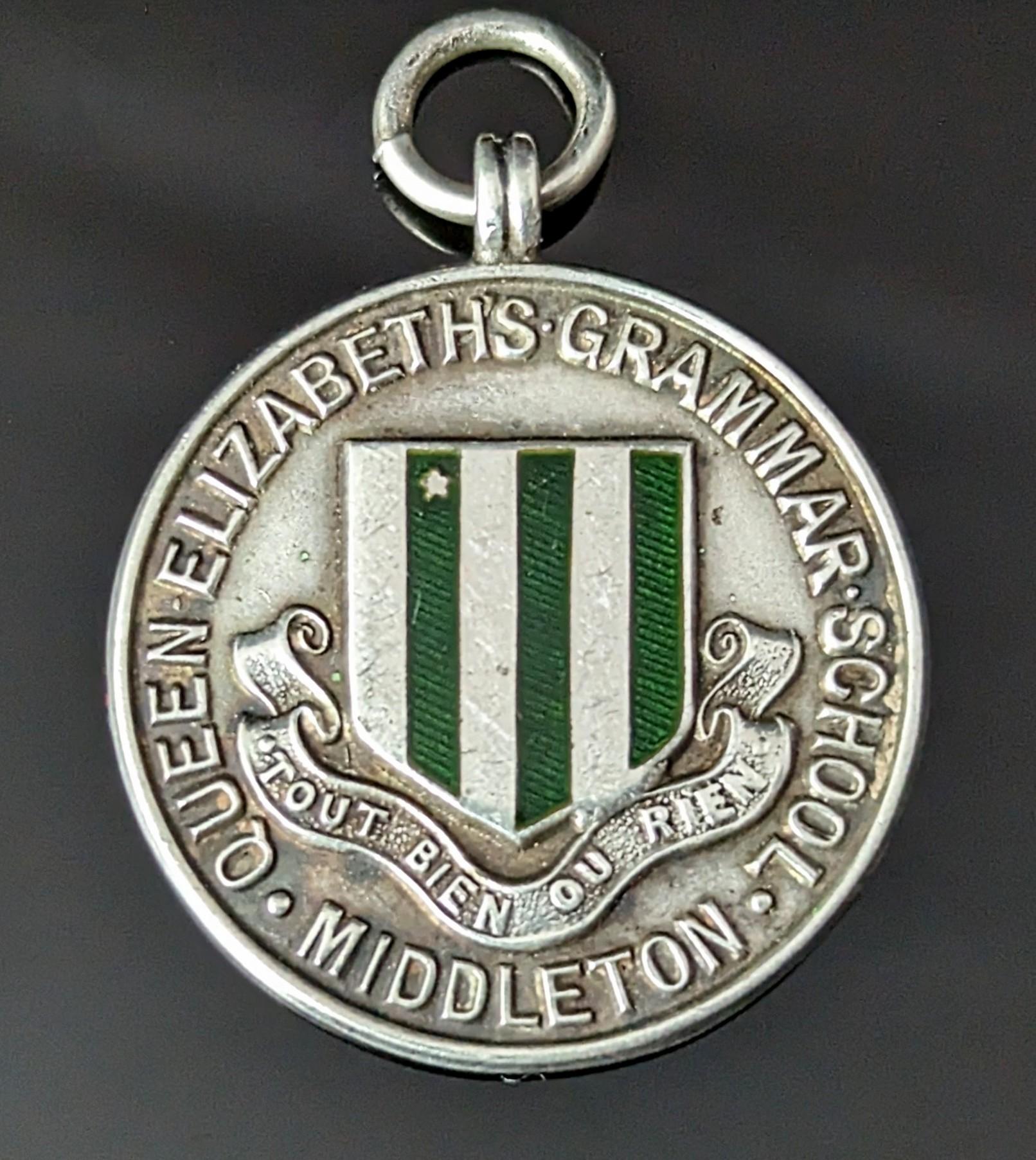 An attractive vintage sterling silver and enamel fob pendant.

It is a circular shaped piece with an attractive forest green enamelled design, the green enamel shield to the front representing Queen Elizabeth's Grammar School with the French text