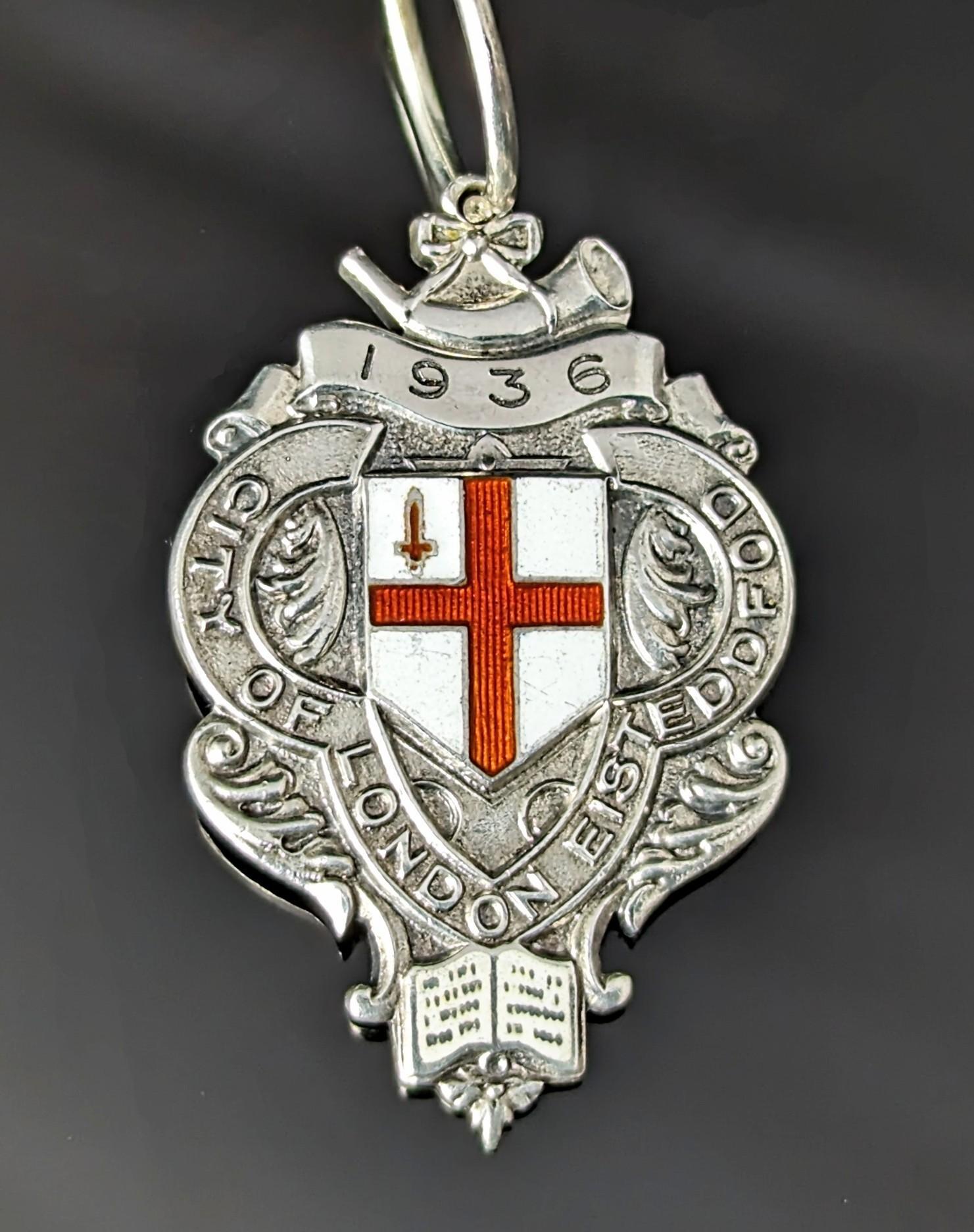An attractive vintage sterling silver and enamel fob pendant.

It is fairly large made from sterling silver and features an enamelled flag the St George Cross in a shield shape along with a small red sword.

Below this is a small enamelled open