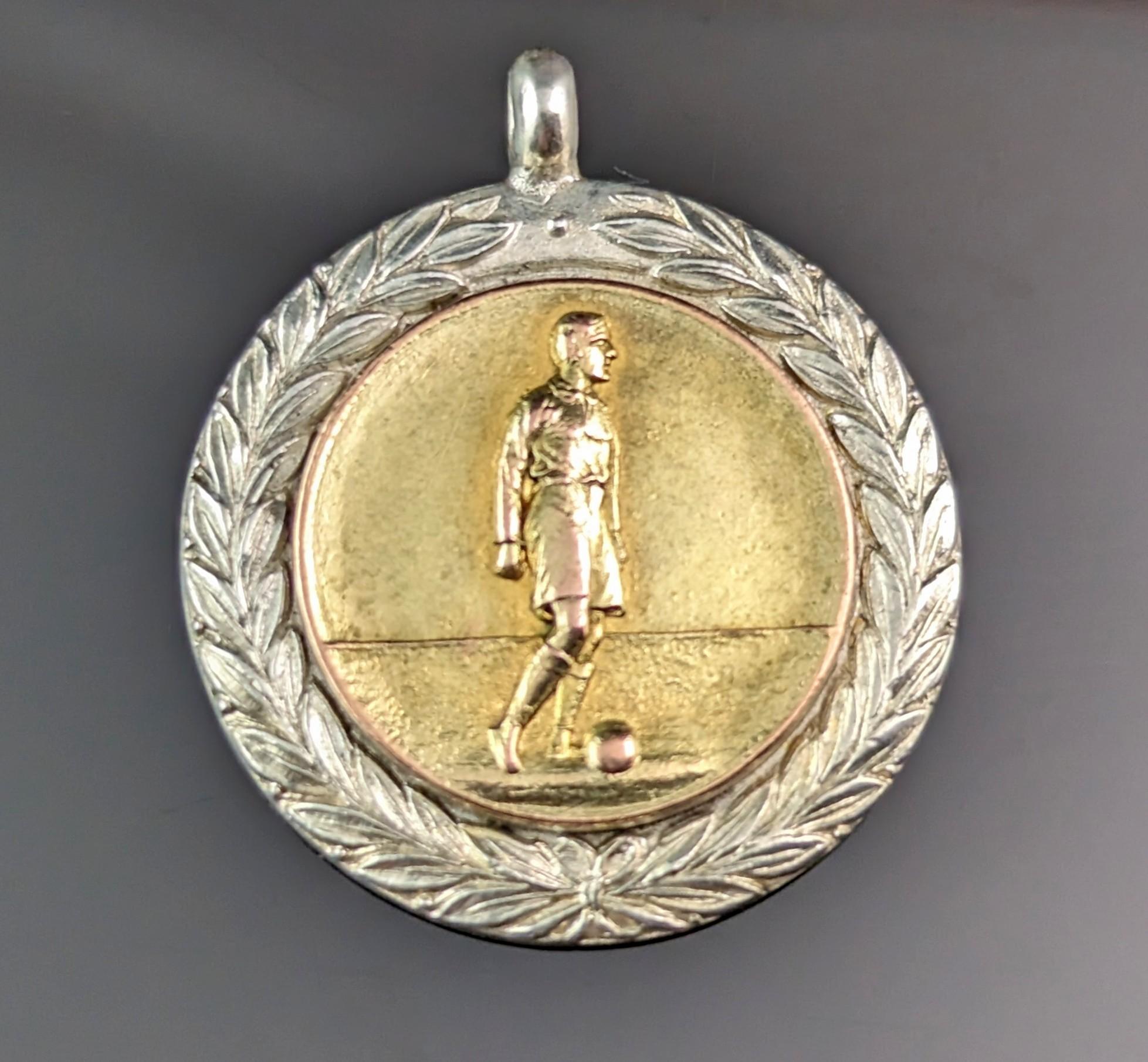 An attractive vintage, Art Deco era silver and gilt silver watch fob pendant.

It is a circular shaped fob with a Laurel wreath border in silver and the central area decorated with a repousse figure of a man with a football and gilded in a rich