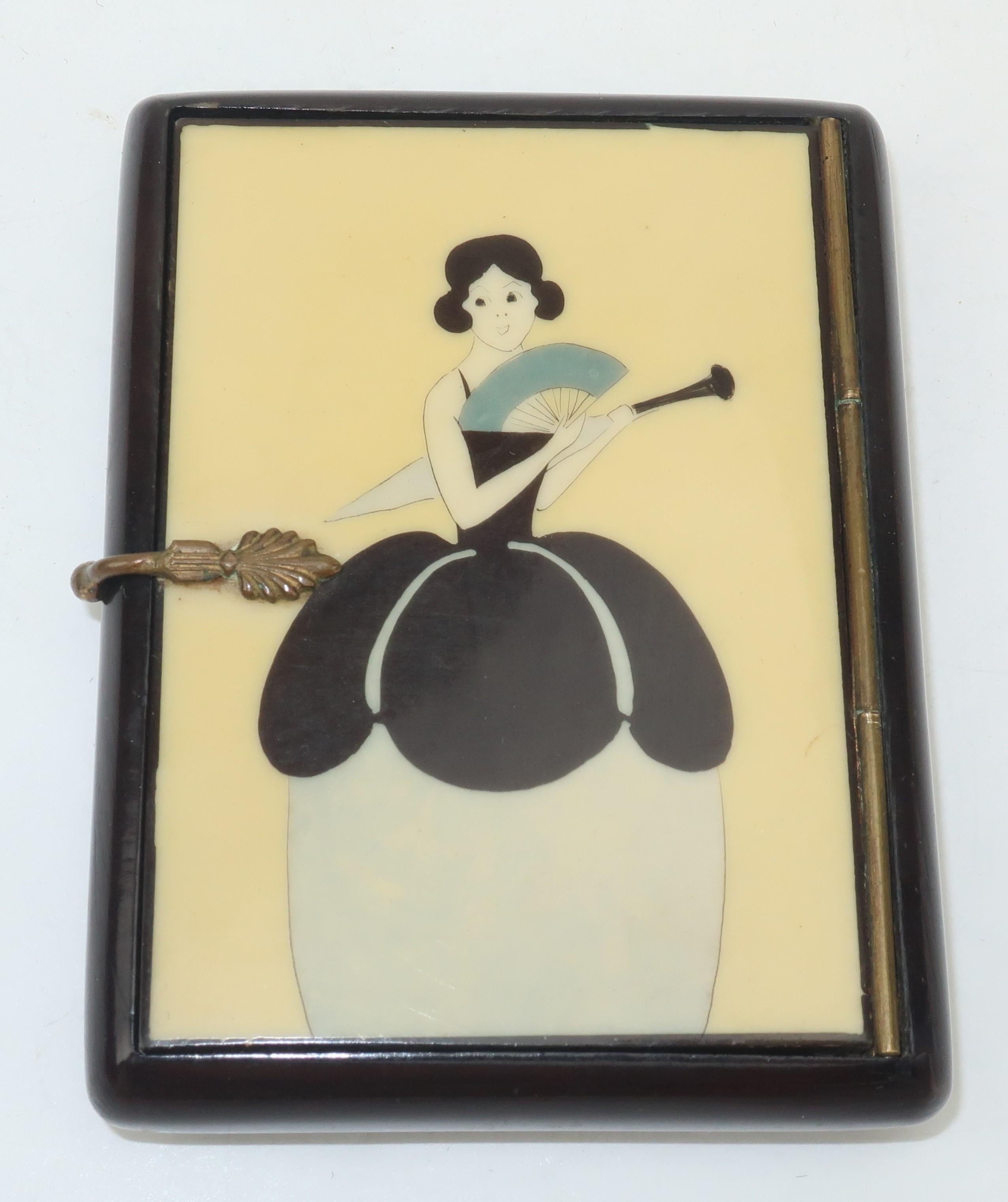 Sweet and petite!  This Art Deco era lacquered wood box features a decorative metal closure and a feminine figural design depicting a lady with fan and parasol all in shades of black, ivory and dove gray.  The interior is lined with a dark brown