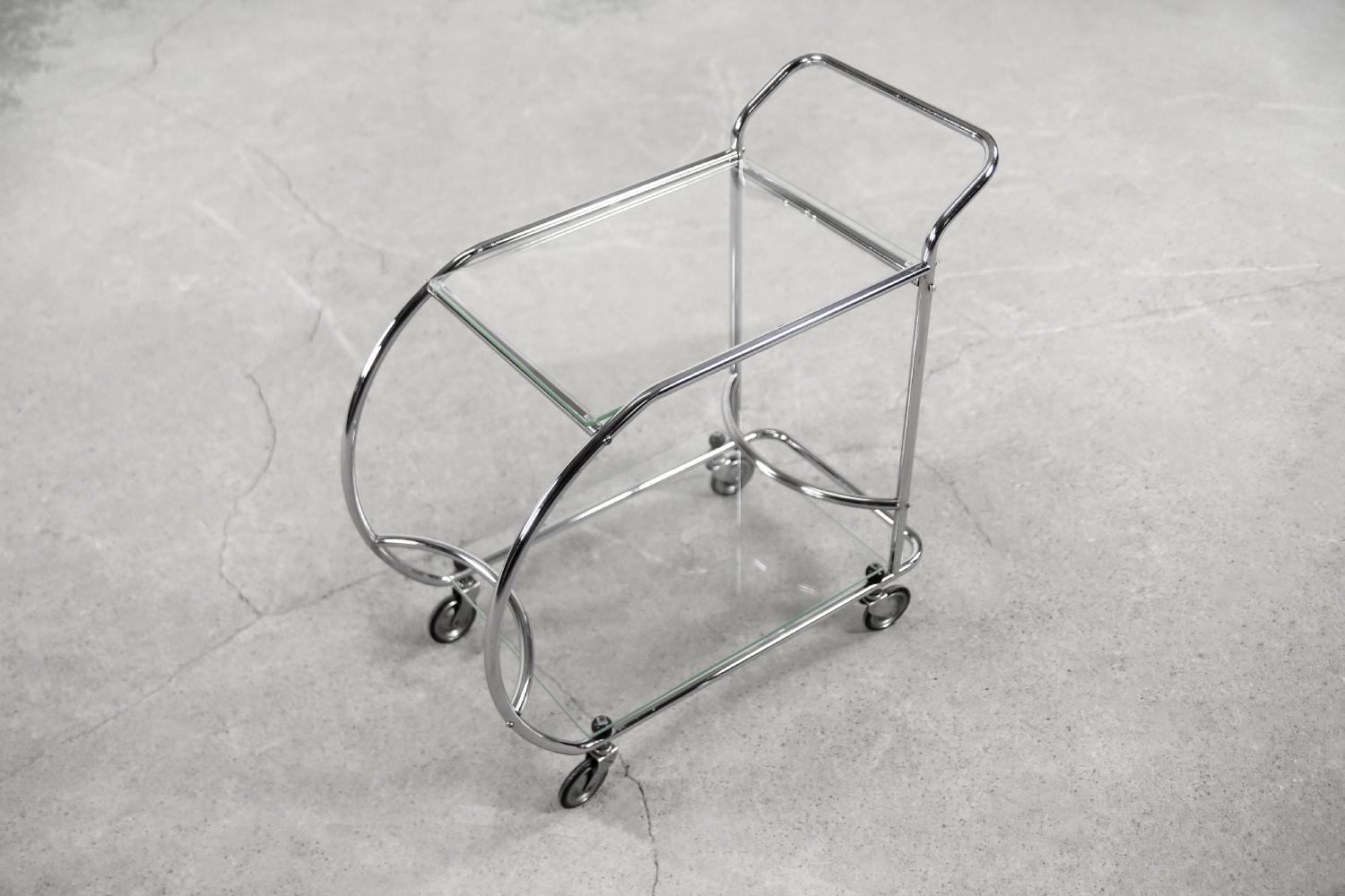 This small and light bar table was manufactured during the 1950s. Its form refers to the pre-war Art dèco style. The streamlined frame is made of chromed tubulars steel. There are transparent glass tops on two levels. Comfortable handle and wheels