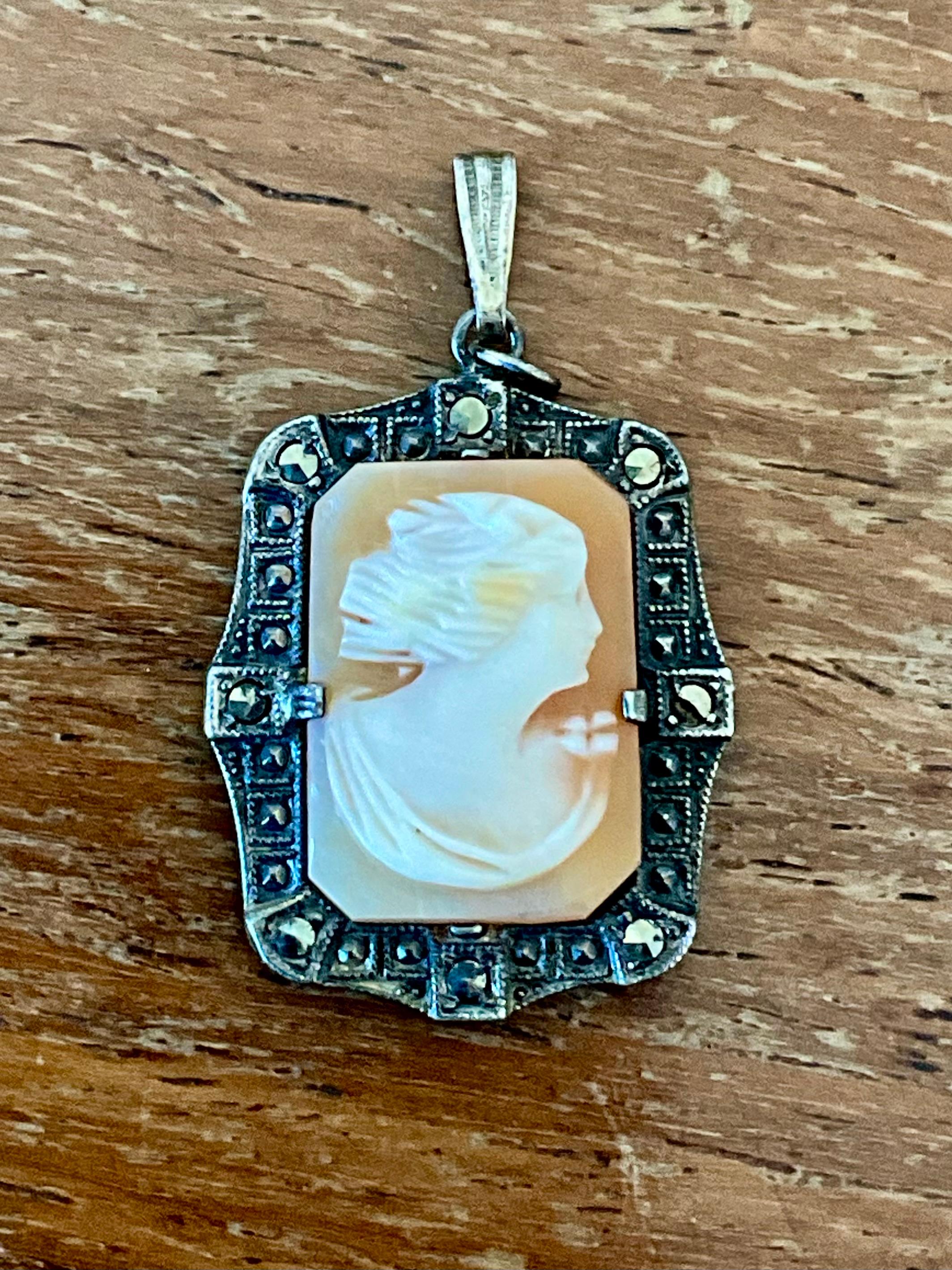 Questo ciondolo a cammeo intagliato in argento Sterling Art Deco vintage cattura magnificamente l'eleganza e la raffinatezza geometrica degli anni Venti. Sapientemente intagliato a mano in vera conchiglia, il cammeo presenta un raffinato profilo
