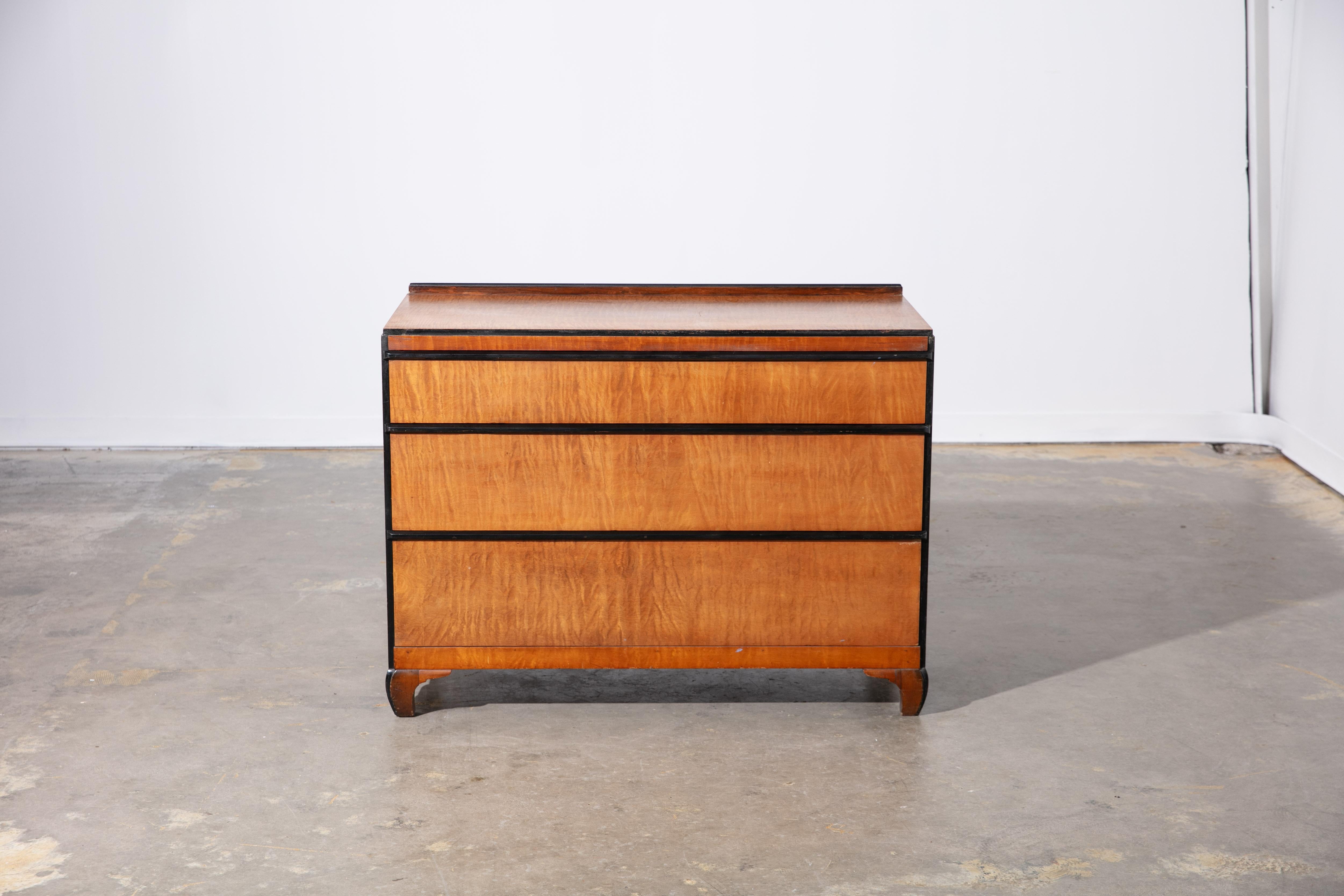 Comò d'epoca a 3 cassetti in stile Art Déco con dettagli ebanizzati sul bordo. Nel complesso è in buone condizioni, con lievi perdite e graffi. 3 ampi cassetti con venature del legno color miele, appoggiati su gambe ricurve.