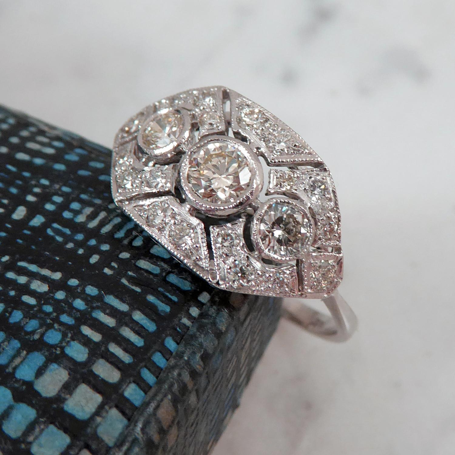 A mid-20th century diamond set dress ring consisting of three centrally set, fully rub over set, round brilliant cut diamonds. The diamonds are inset against a hexagonal-shaped white surround, grain set with a total of 18 round brilliant cut