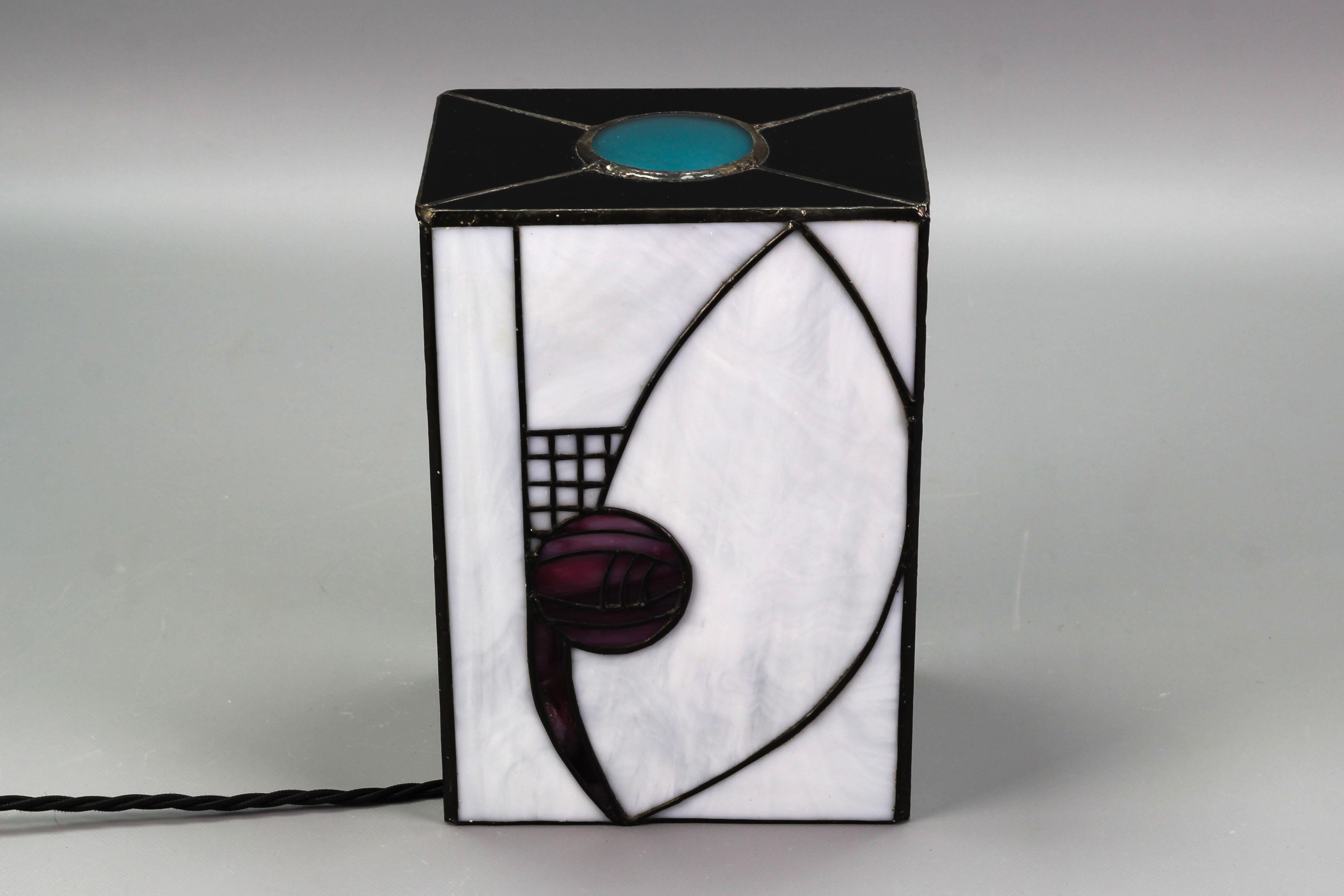 Beautiful Art Deco-style stained glass lamp in black and white with geometrical accents in purple and turquoise. The lamp looks wonderful as well as lit as unlit. When lit, the dark glass looks very dark purple.
One socket for E27 (E26) light bulb.
