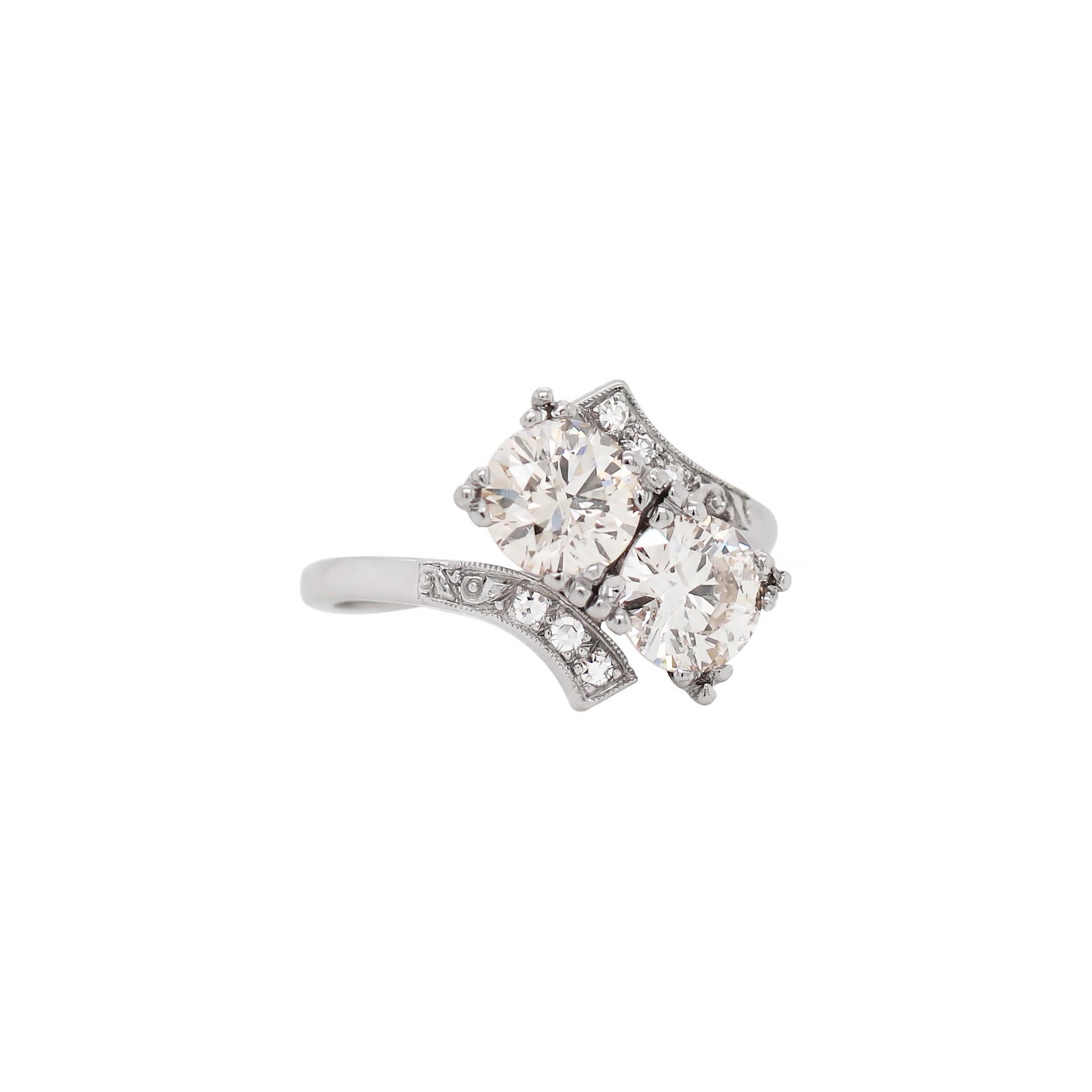 This beautiful Art Deco style two stone cross-over engagement ring features two round brilliant cut diamonds weighing approximately 1.05 carat each, both in a triple four claw open back setting. The two stones are beautifully set within twisted