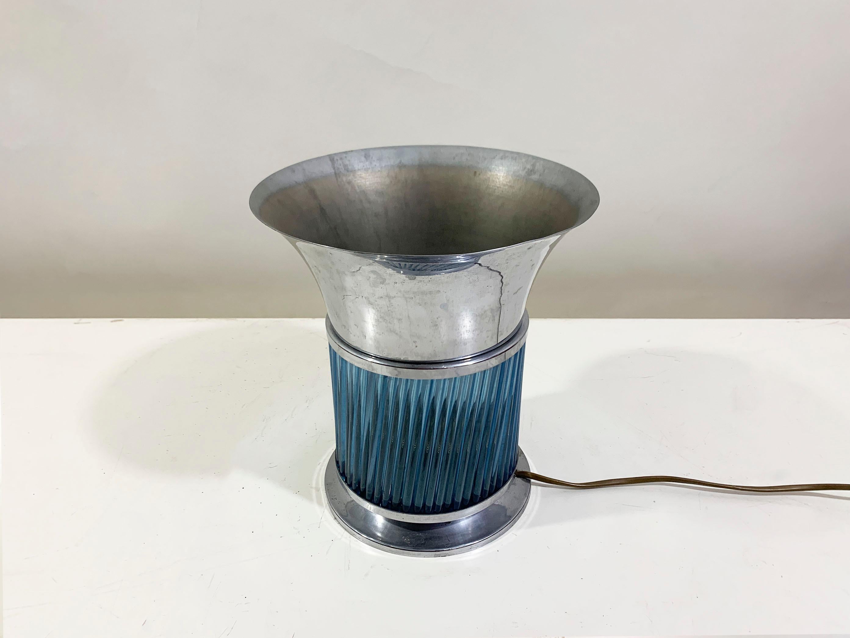La lámpara es un sorprendente ejemplo del diseño Art Déco de los años 30, que encarna la elegancia elegante y las atrevidas formas geométricas características de la época. La base y el cuerpo están hechos de un rico cristal azul que brilla con una