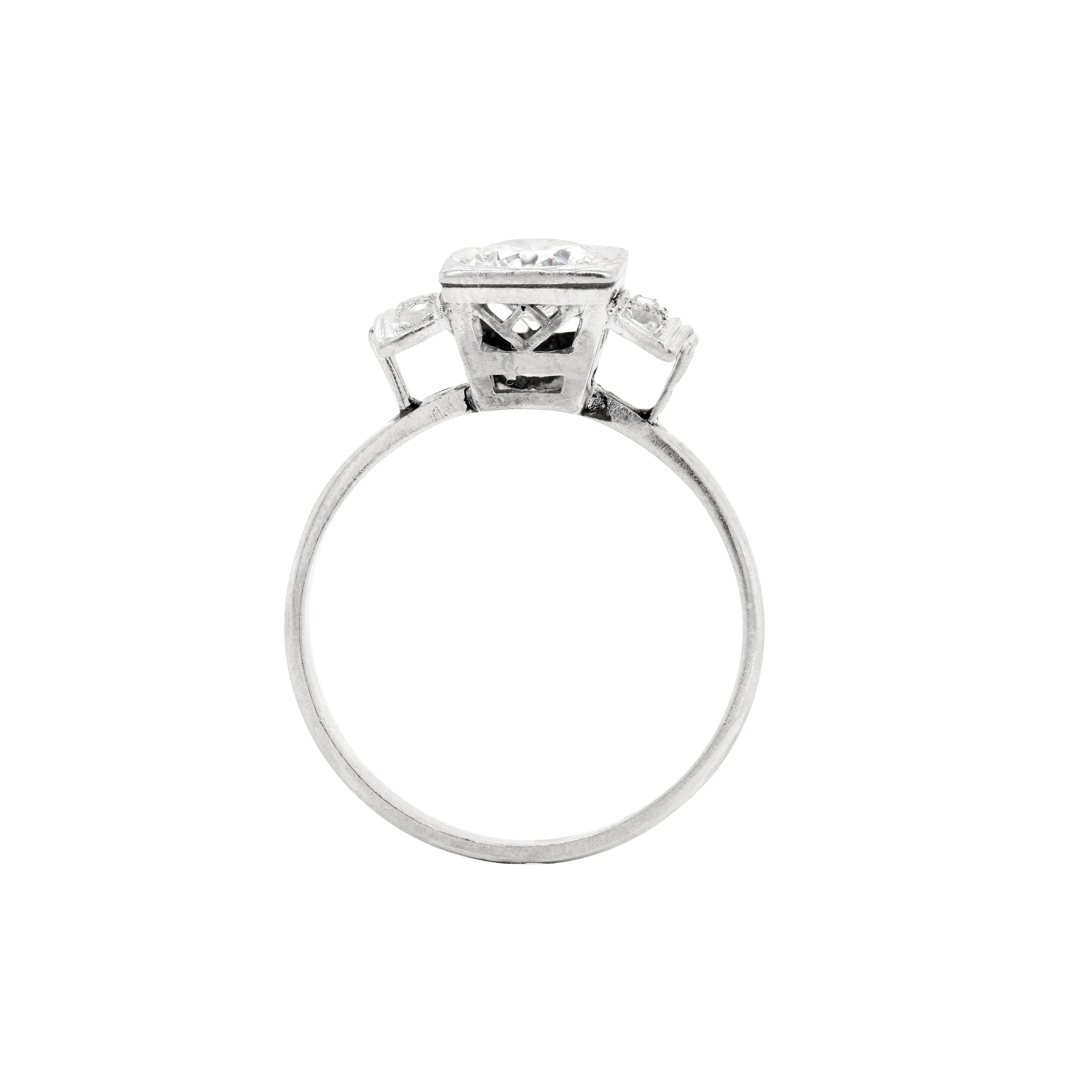 This wonderful Vintage engagement ring features a beautiful transitional cut diamond grain set into a hexagonal bezel within a high square box mount. The piece is further designed with diamond set step shoulders that lead past an open work gallery