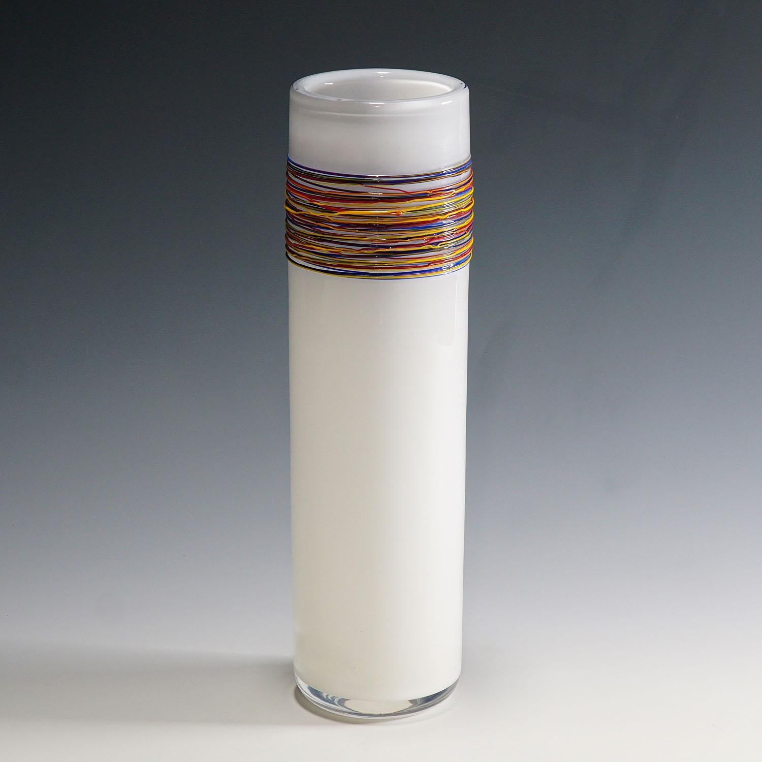 Eine Vase aus Kunstglas, entworfen und hergestellt in der Glasfachschule Zwiesel in Bayern. Opakweißes Glas mit Klarglasüberfang, verziert mit heiß verschmolzenen Glasstufen aus rotem, gelbem und blauem Opakglas. Deutschland ca. 1980er Jahre. Auf