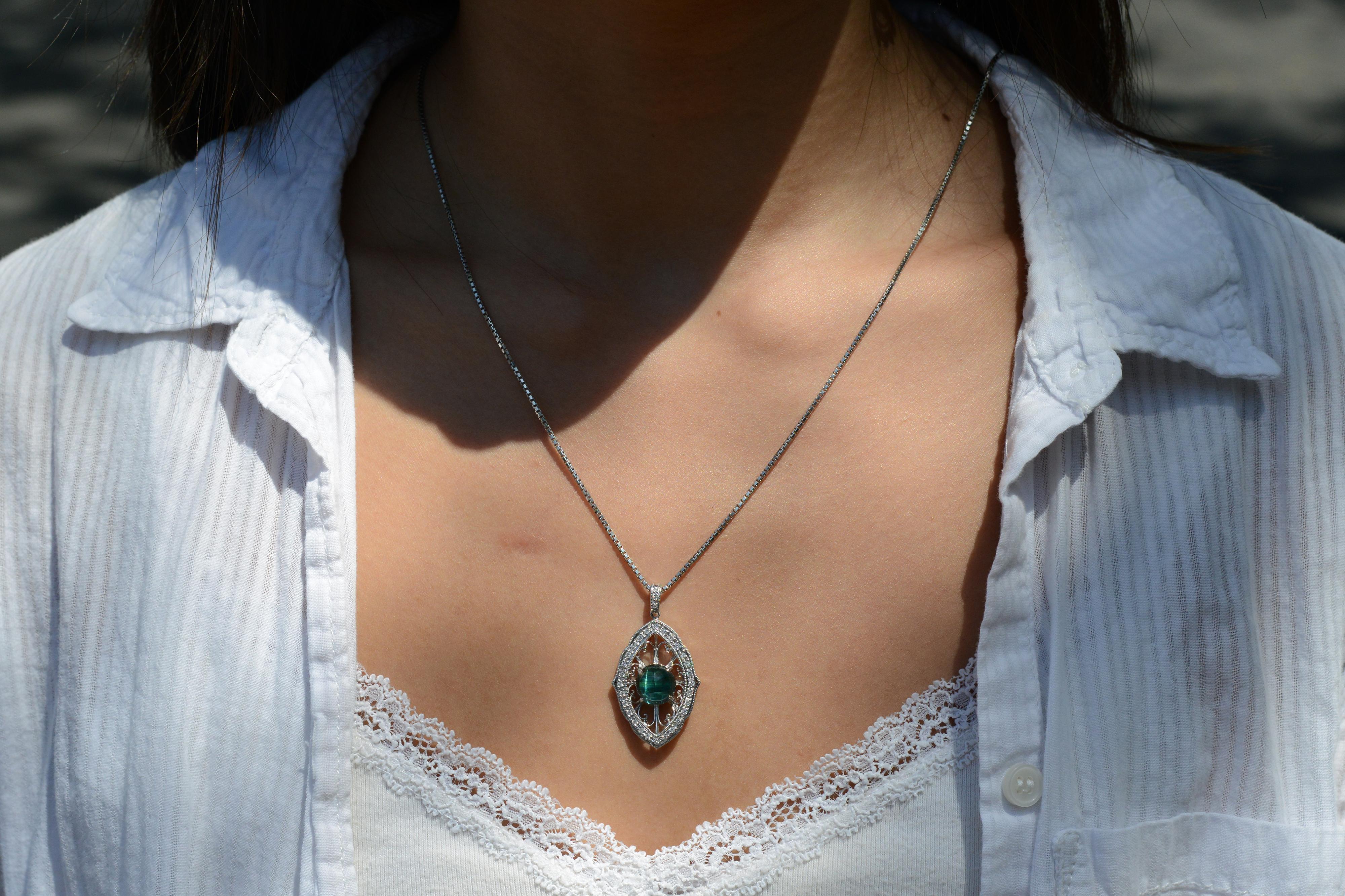 Embrace the revival of the great Art Nouveau era and complement your jewelry collection with this stunning, blue-green indicolite tourmaline pendant. Crafted from platinum with exquisite scrolling vines and milgrain, this necklace showcases a unique