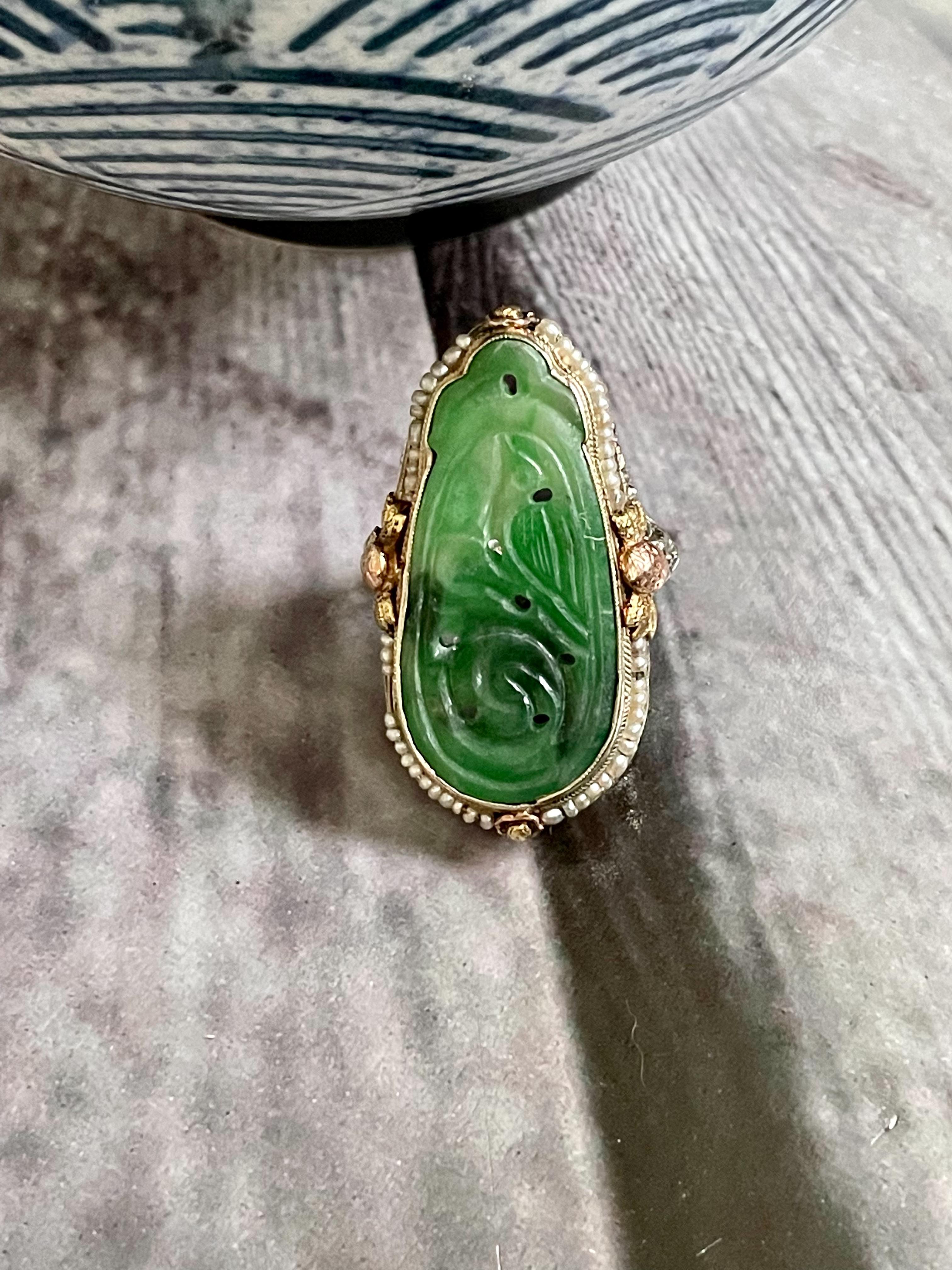 Dieser Ring ist mit einem tropfenförmigen, skulptierten Jadestein besetzt.  Er ist umgeben von einem Kranz aus Saatperlen, die alle in eine 18-karätige Gelbgoldfassung eingefasst sind.

Abmessungen:  gesicht - 1-3/8
