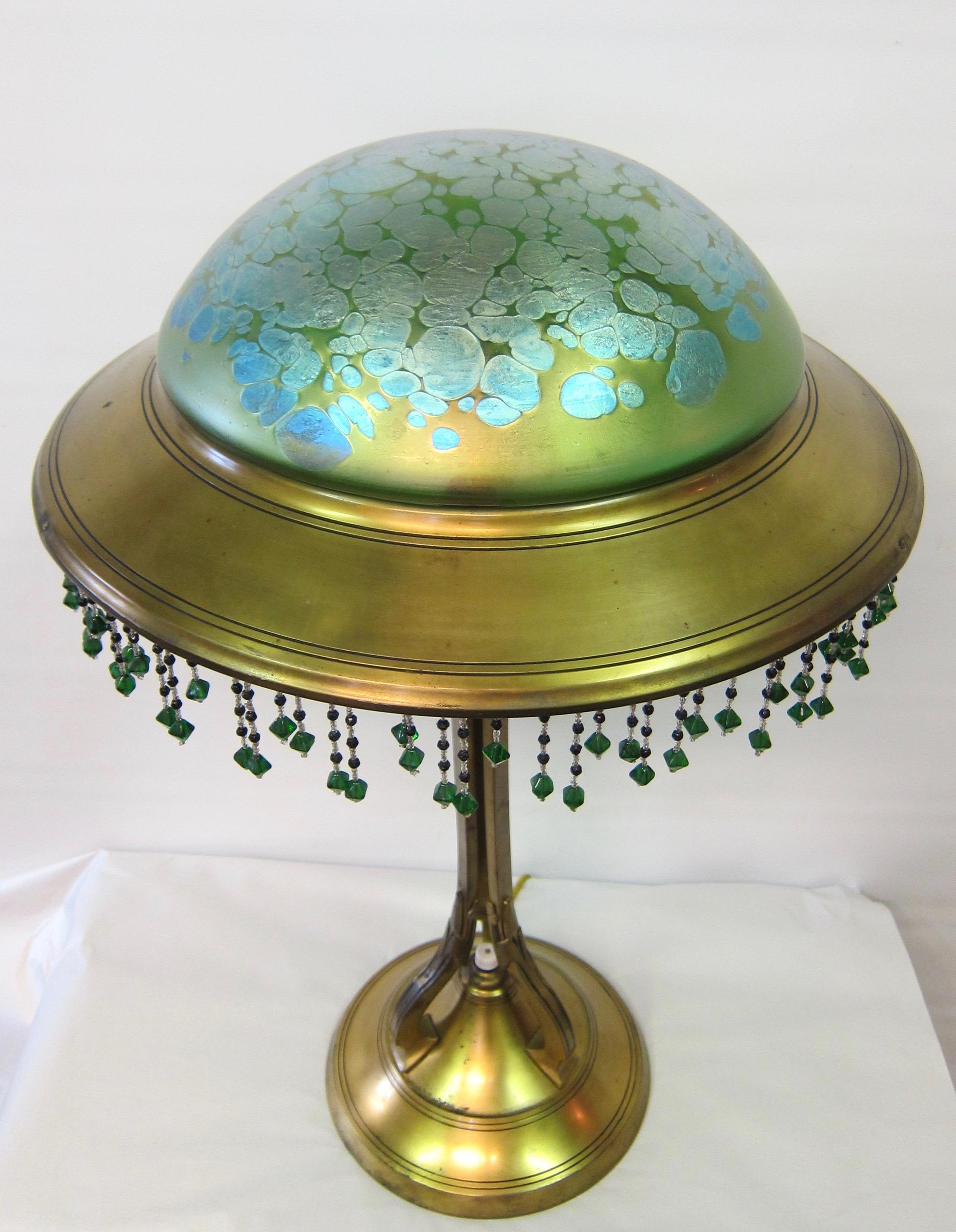 This early 20th century Austrian art nouveau table lamp is from the Loetz factory and has a blue oil spot pattern on a green color dome shape shade. This stunning 12