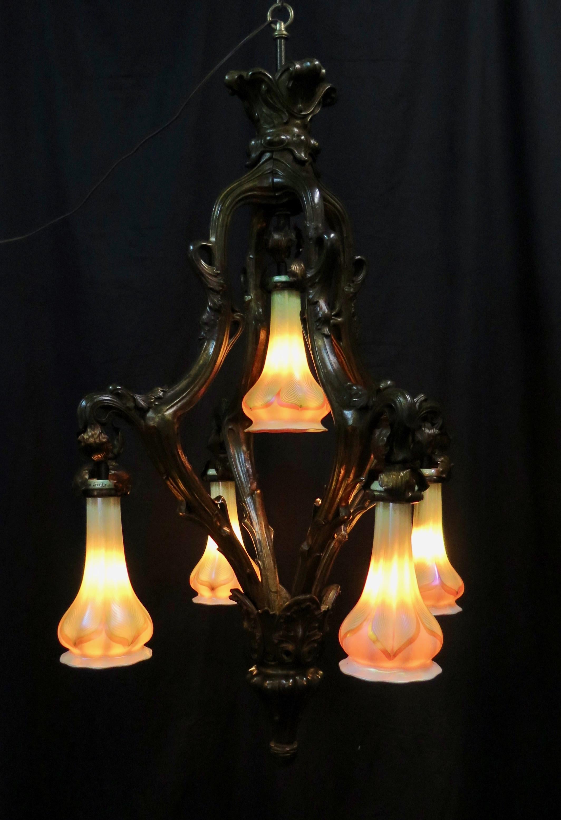 This vintage early 20th century Art Nouveau chandelier is beautifully designed with a brown patinated copper clad body and accented with long art glass shades. The five light ceiling fixture has a flowing floral Art Nouveau motif that embraces its