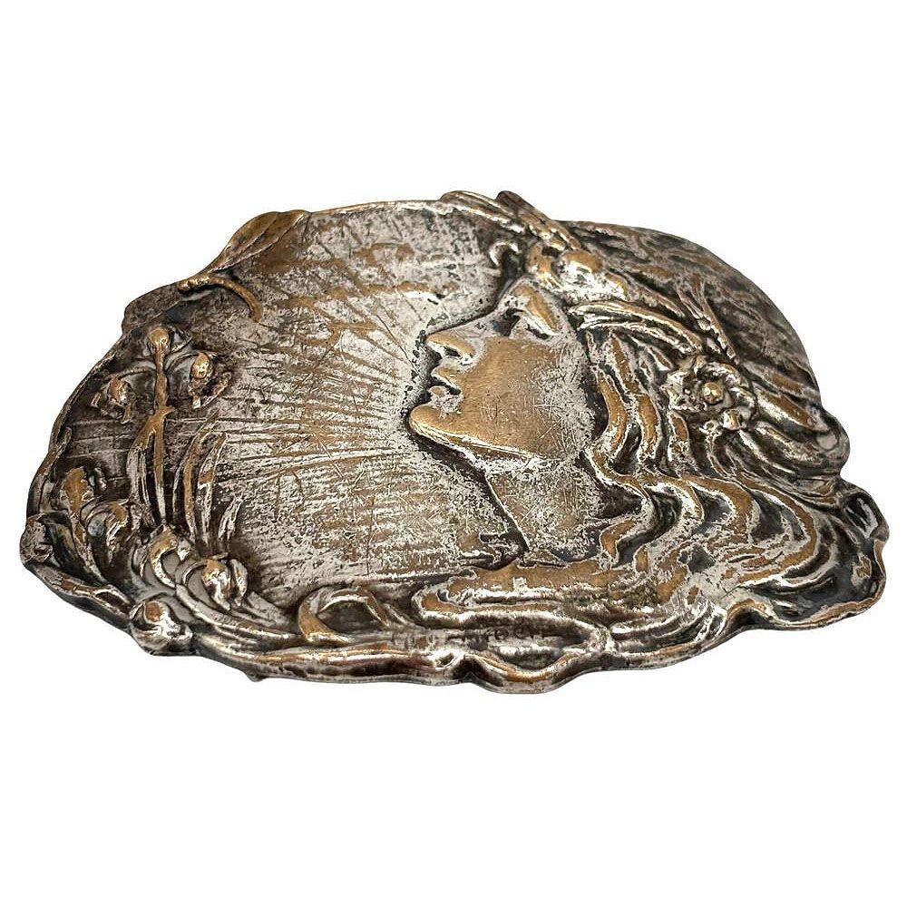 Questa squisita fibbia ispirata ad Alphonse Mucha presenta un accattivante design in stile Art Nouveau, con un ritratto finemente dettagliato di una donna serena incorniciata da un motivo fluente ispirato alla natura. Realizzata in ottone con