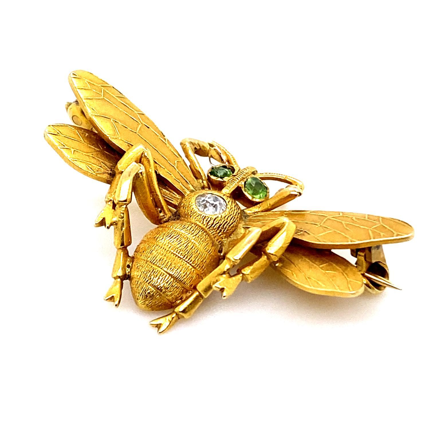 A vintage Art Nouveau style bee brooch pin set in 18 karat yellow gold.

Designed in yellow gold, its head is set with two brightly hued round cut peridots for eyes. The thorax of the bee is set to its centre with a single old cut diamond of 0.20